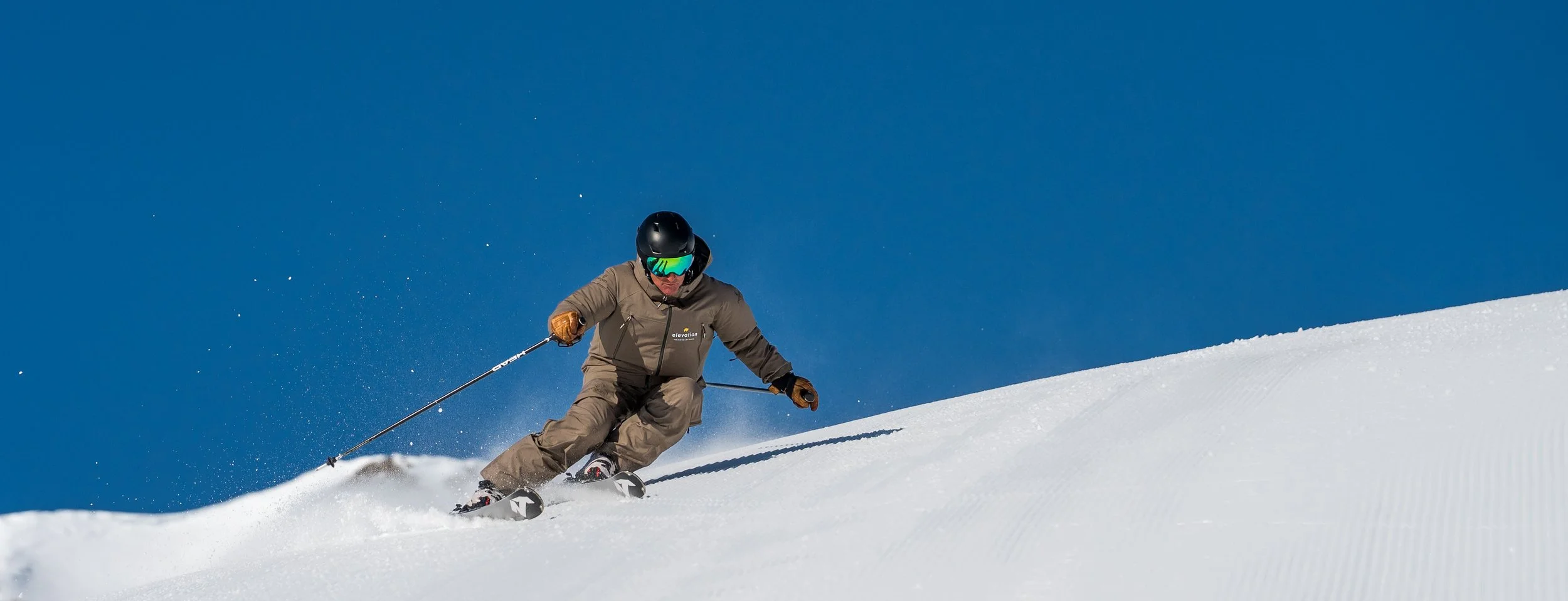 image of ski instructor skiing carved turn with blue sky and mountains in background