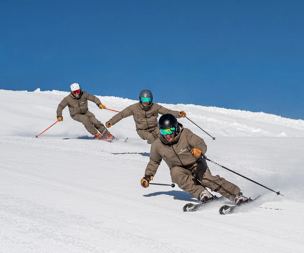 image of 3 skiers carving on a piste with blue sky in the background
