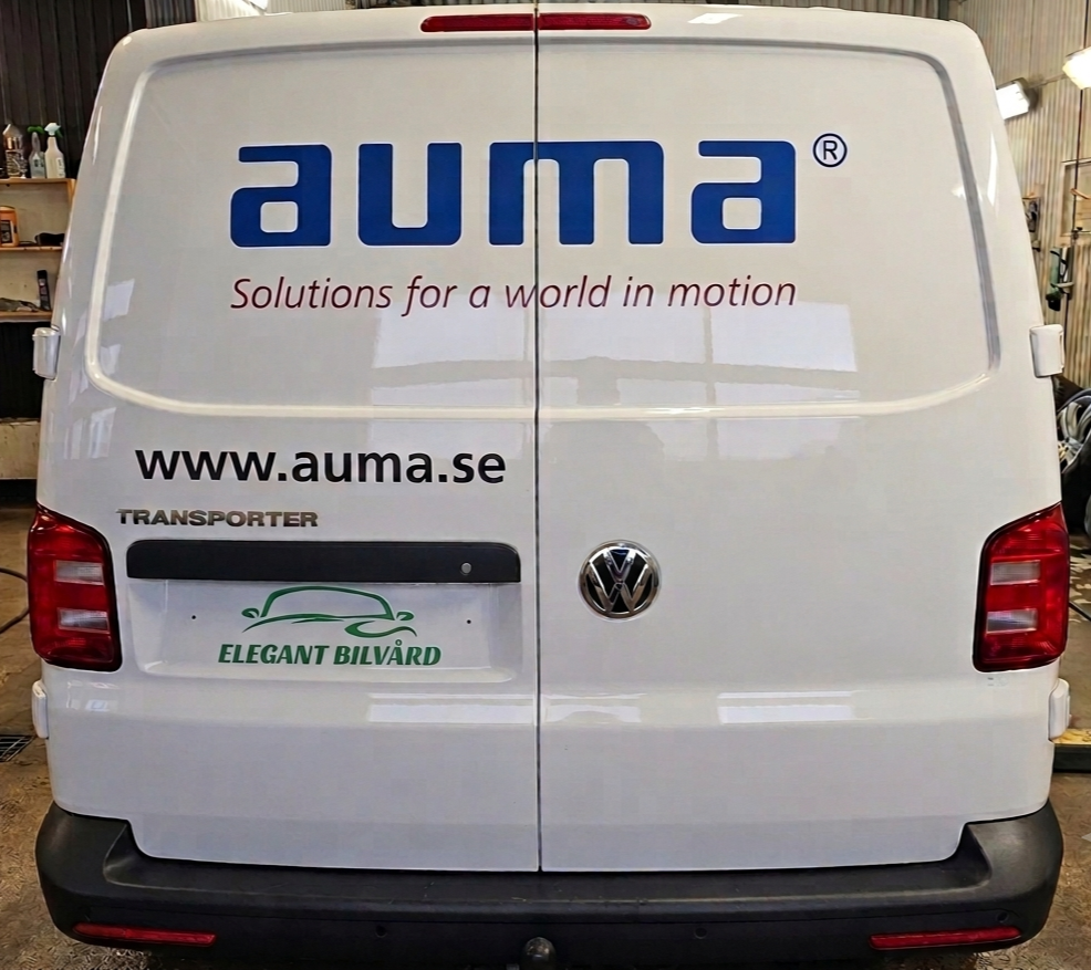 Framsidan av en vit Volkswagen transportbil med företagsloggor och text på dörrarna, inklusive "auma", "Solutions for a world in motion", "www.auma.se", och "Elegant Bilvård".