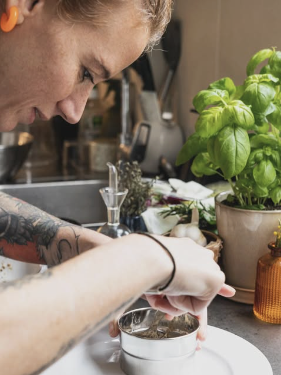 Une personne tatouée en train de préparer une infusion dans une tasse.