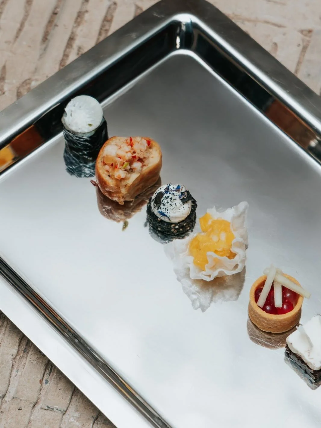 Assortiment de sushis sur un plateau en métal, incluant sushi enroulé, nigiri, et amuse-bouche variées.