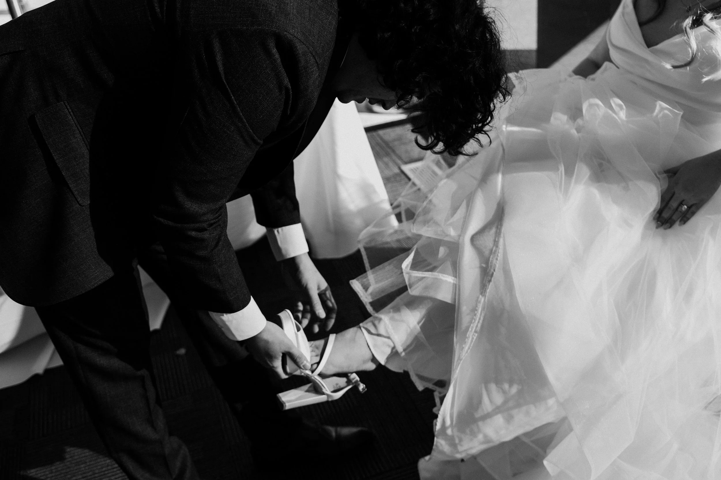 A man in a suit is helping a woman in a wedding dress with her shoes.