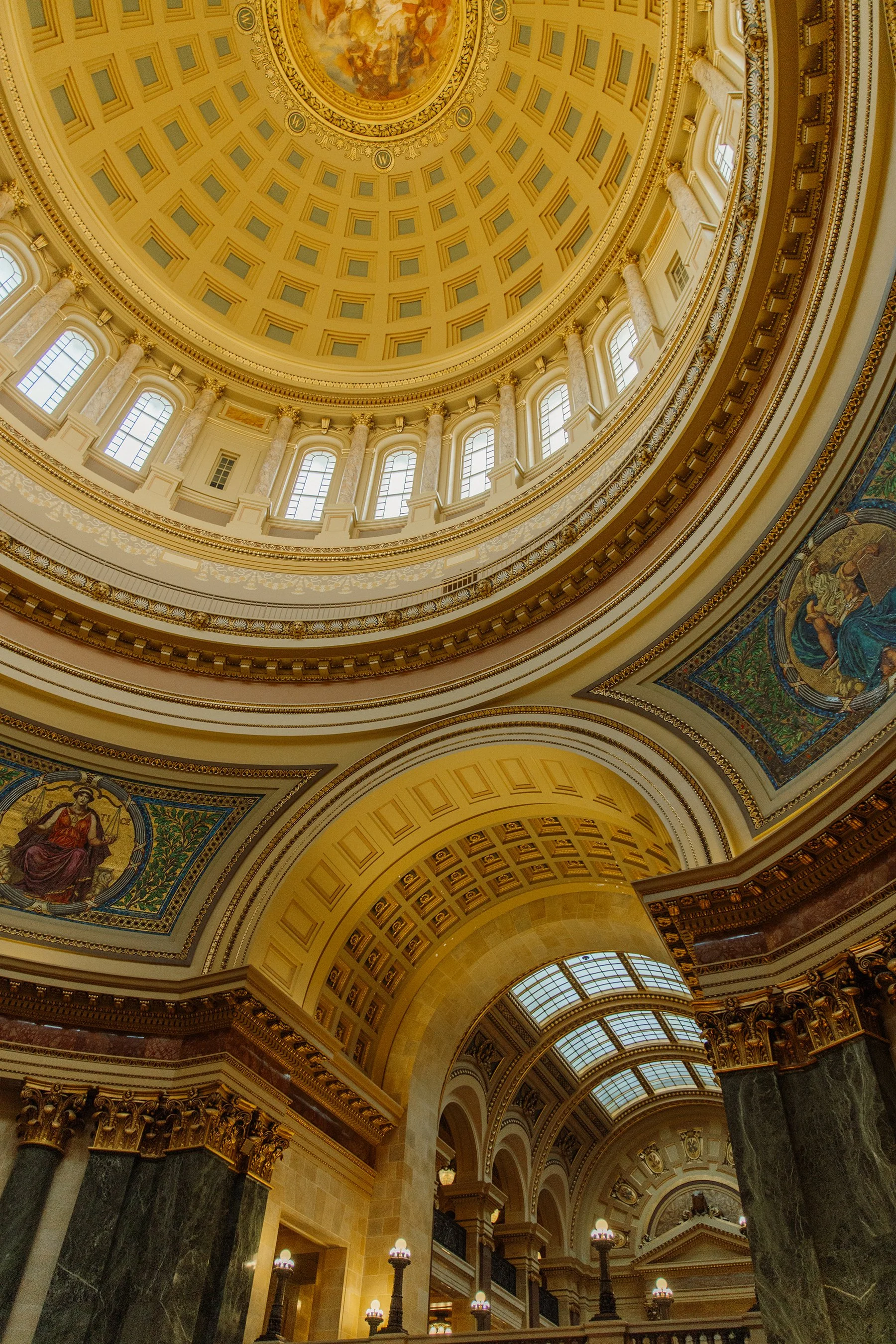 Interior view of a grand domed ceiling with ornate architectural details, columns, and stained glass windows in a historic building.