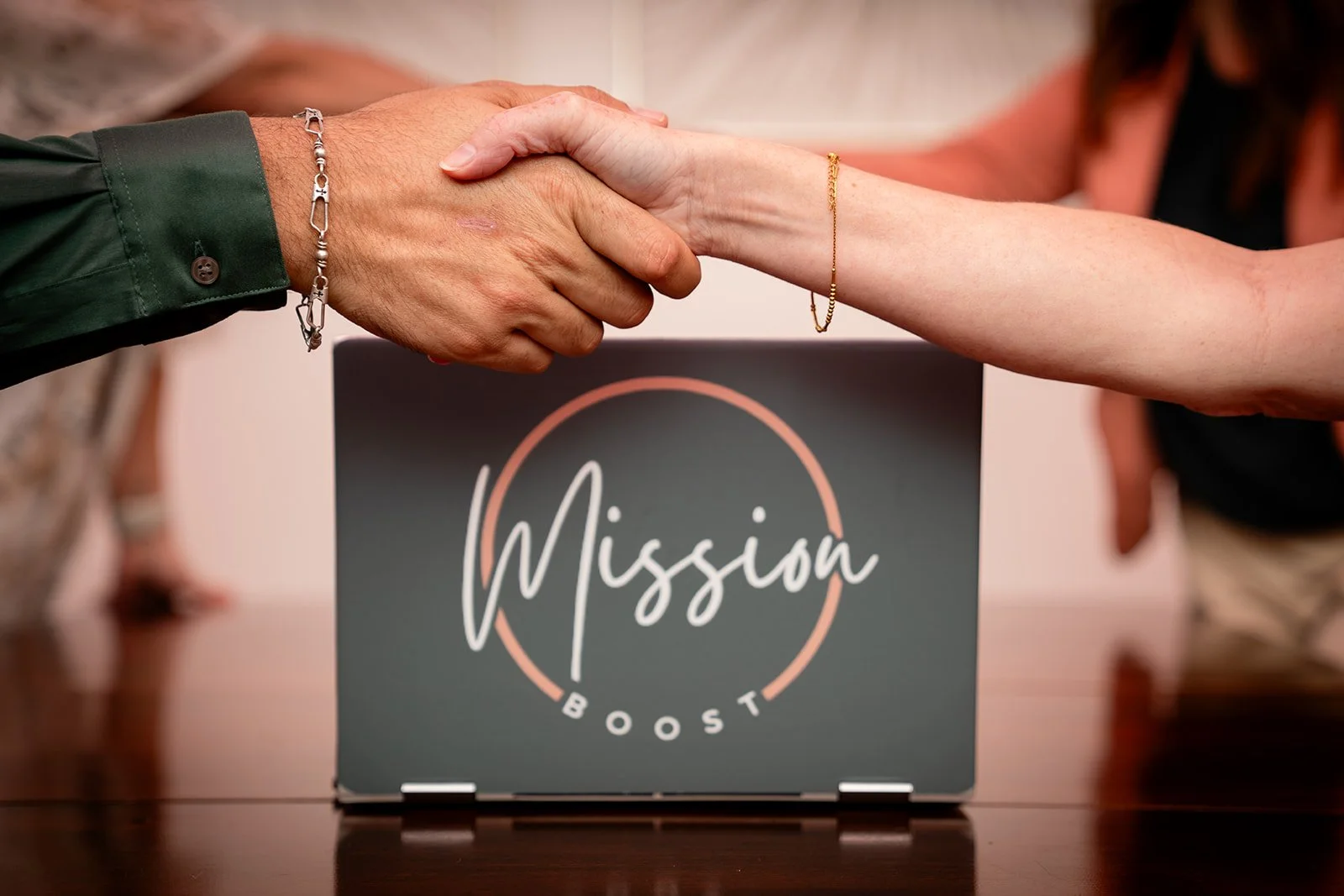 Two people shaking hands over a laptop with "Mission Boost" on the screen.