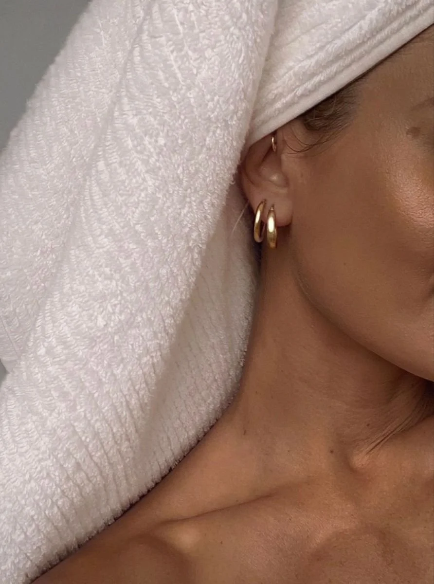 Close-up of a woman with a towel wrapped around her head, showing earrings and part of her face and neck.