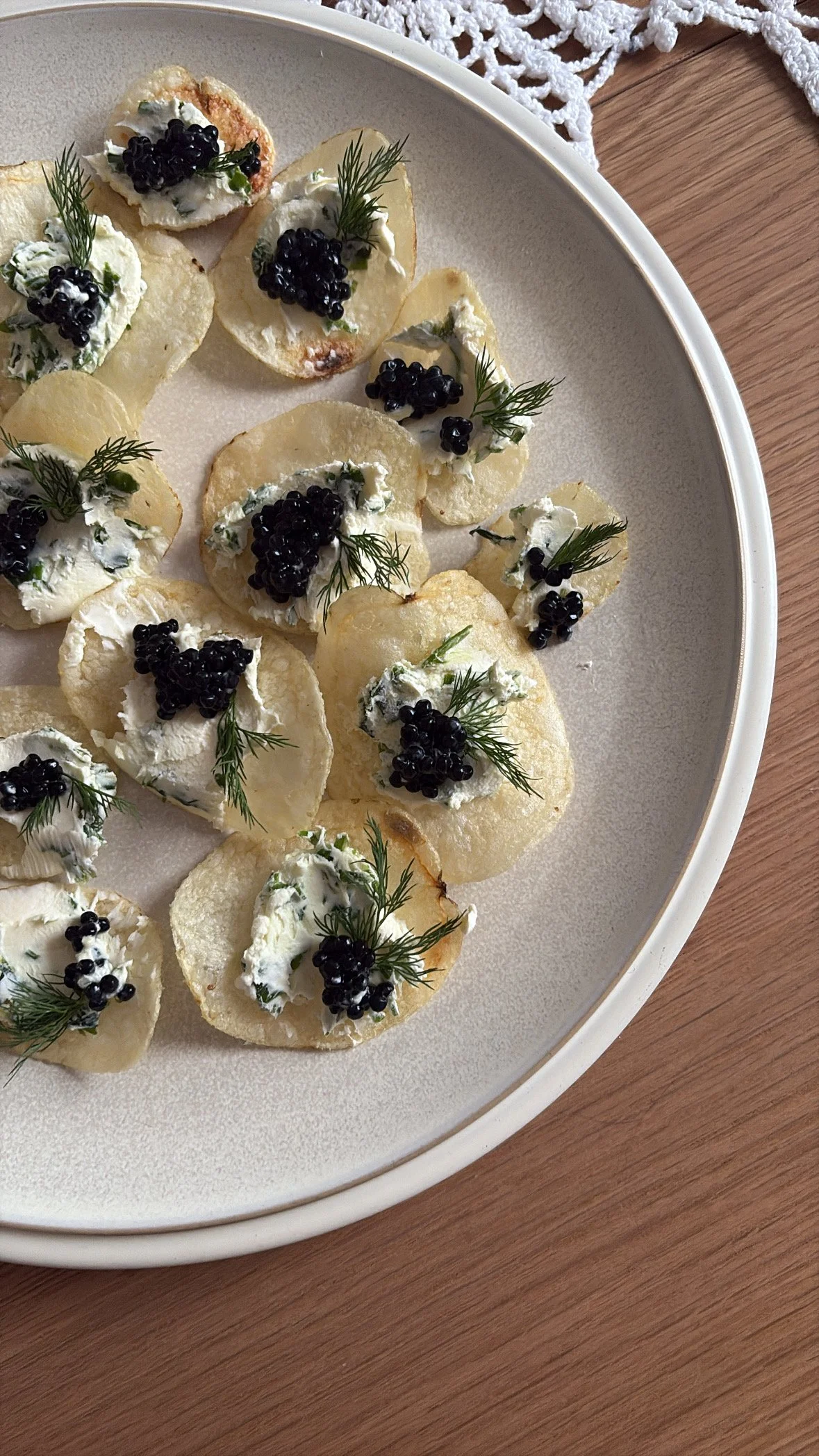 Crispy potato chips topped with creamy herb spread, black caviar, and small sprigs of dill on a beige plate.