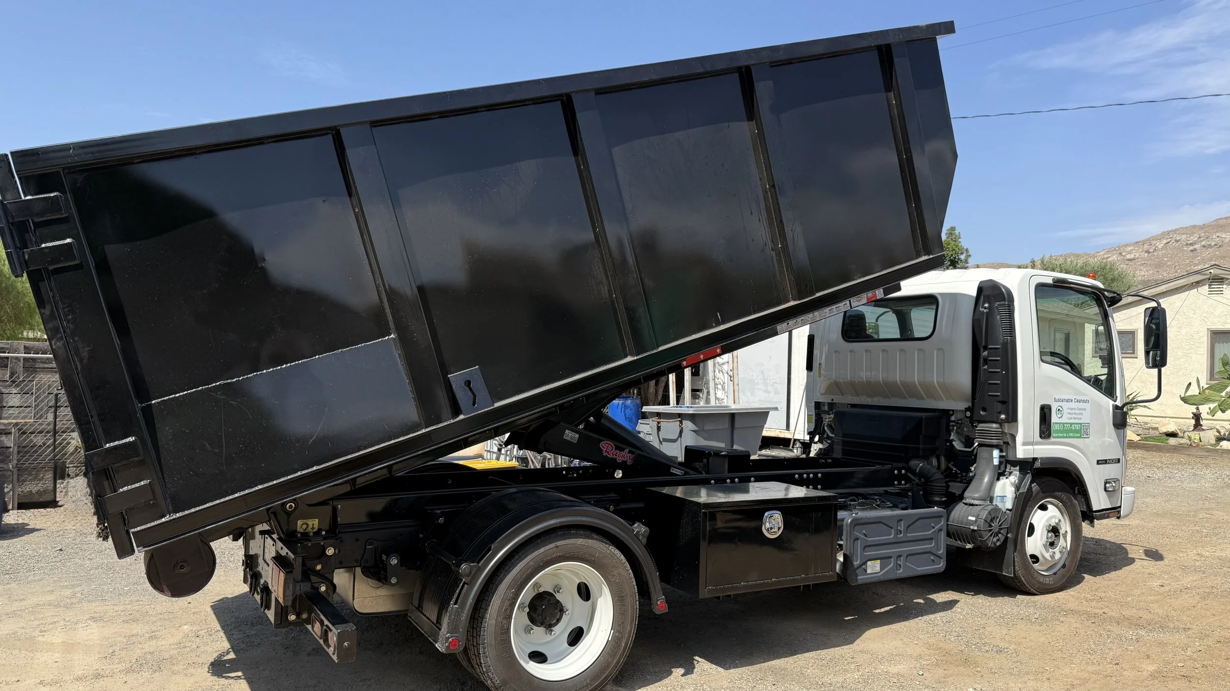 Roll-off truck lifting a black dumpster container during a residential pickup.