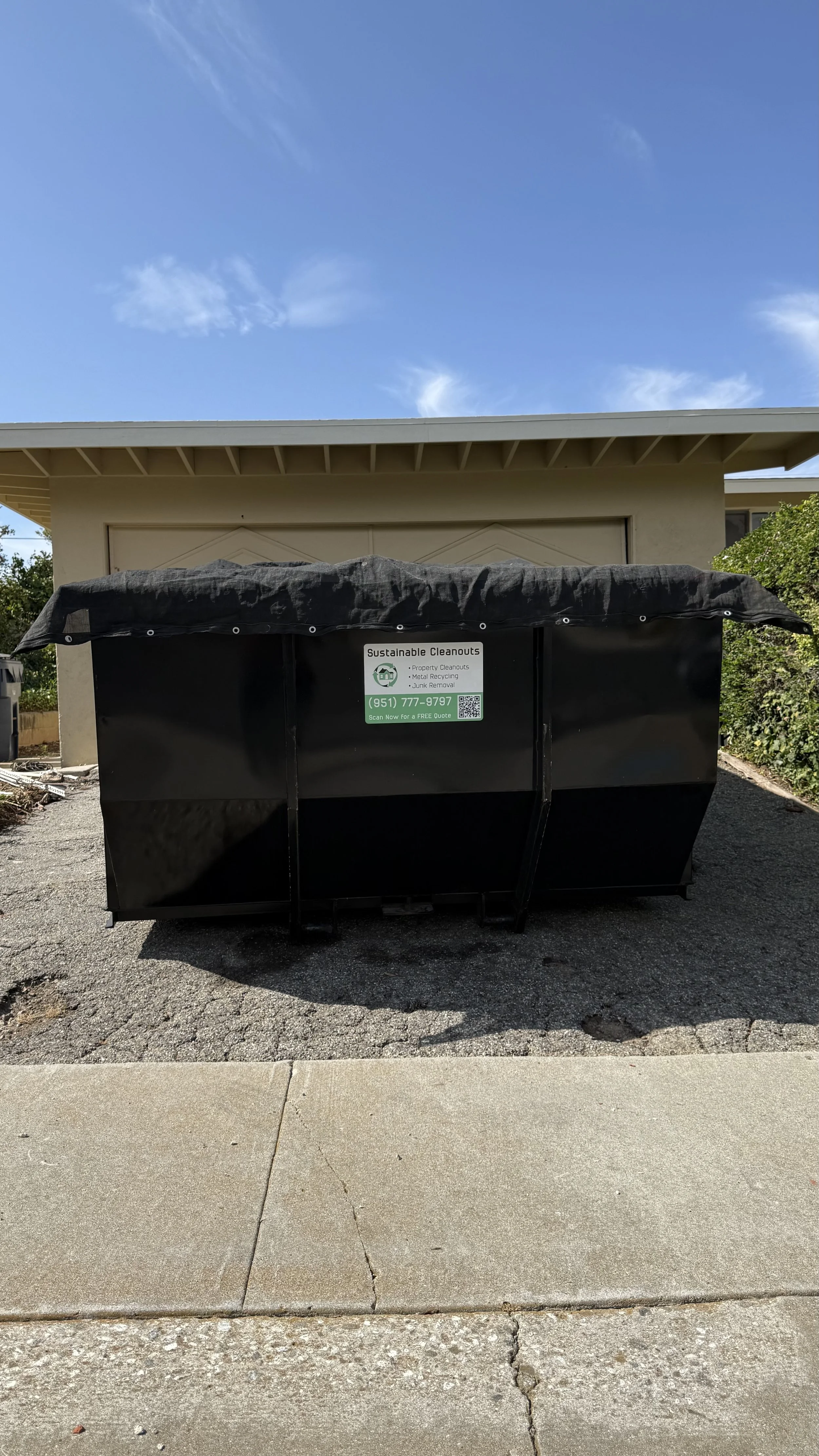 Black roll-off dumpster positioned at the curb for a residential cleanup project.