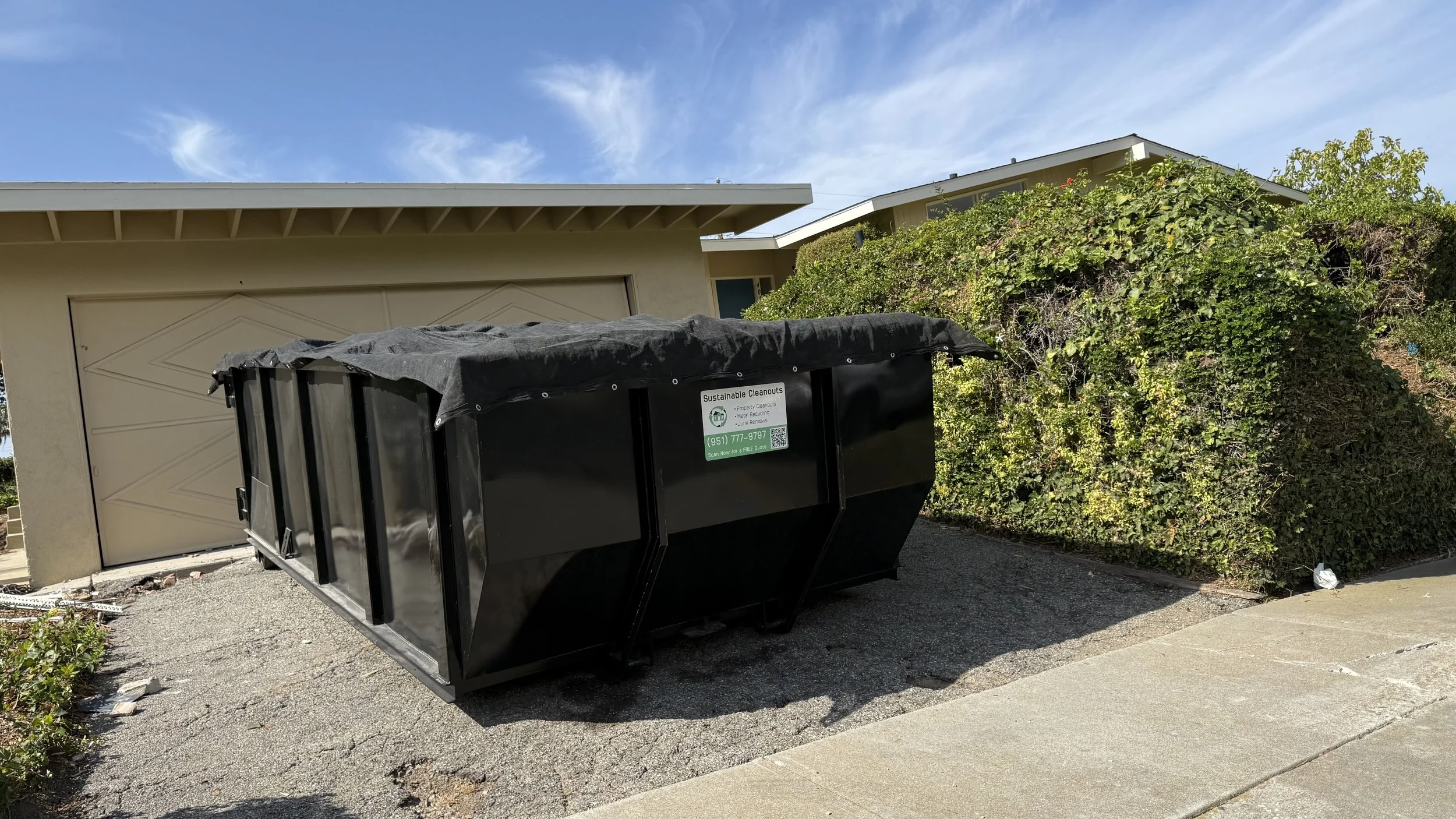 Black roll-off dumpster beside a residential driveway for a cleanup project.