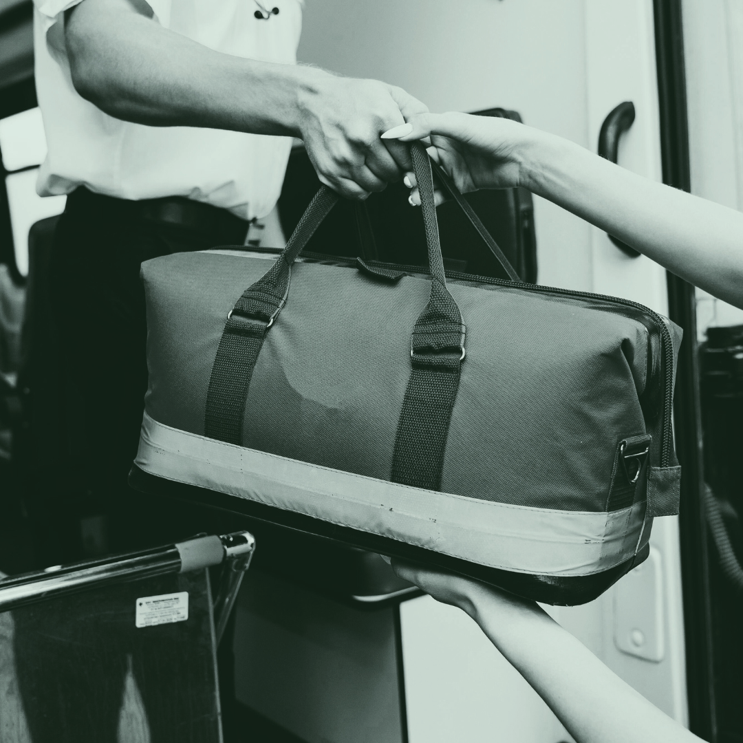 Person handing over a duffel bag to another person on a bus or train.
