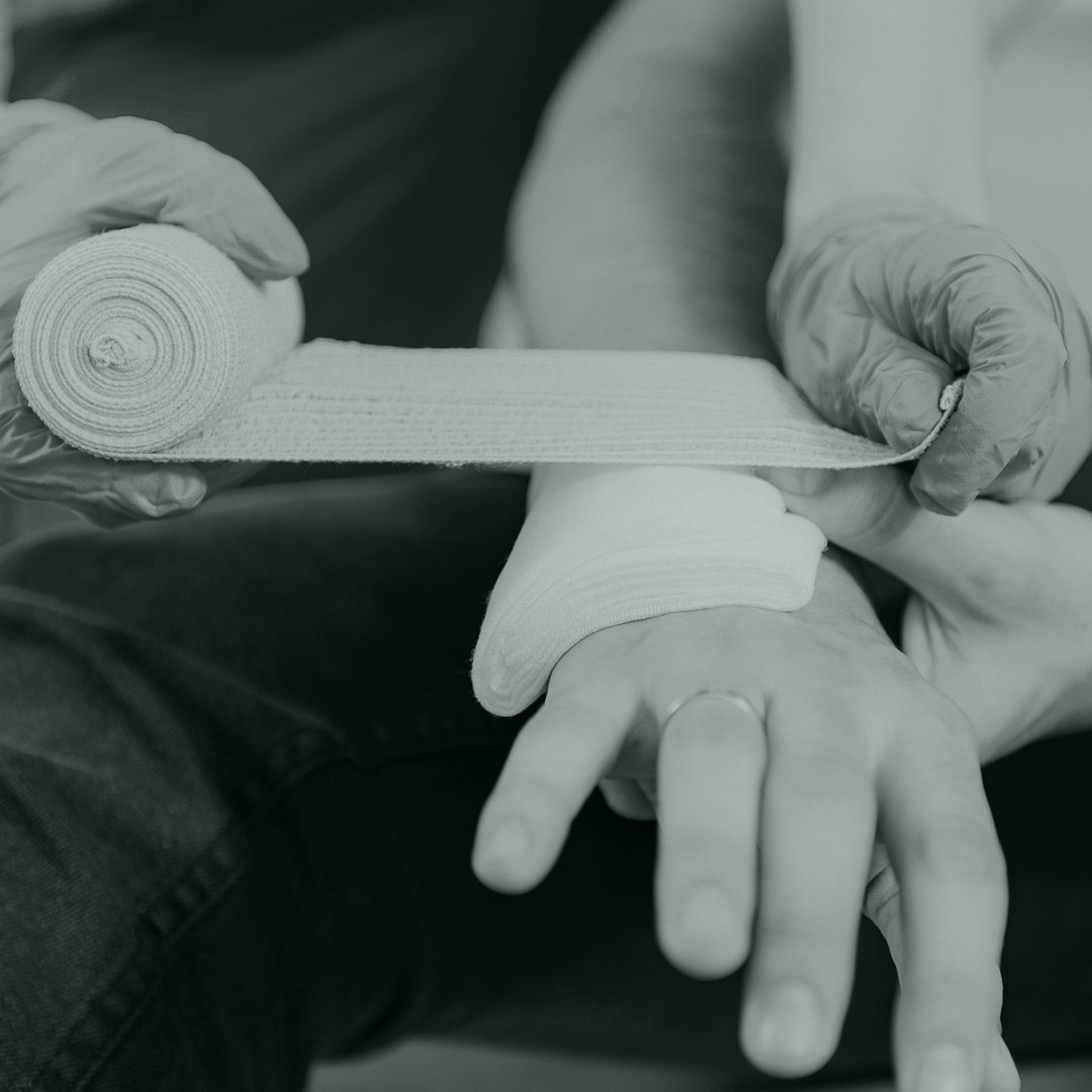 A person wearing gloves applying a bandage to another person's wrist.