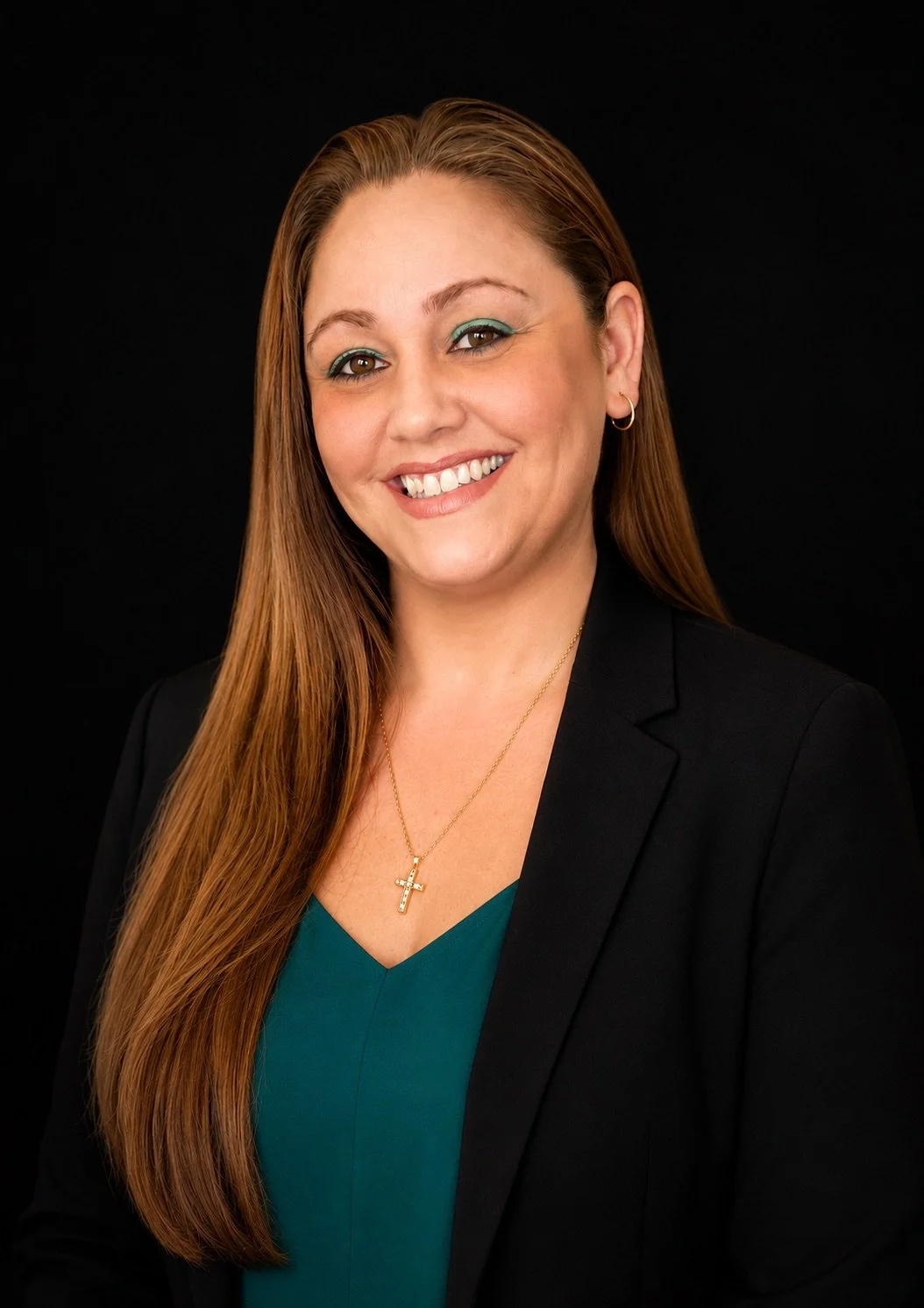 A woman with long reddish-brown hair, smiling, wearing a colorful dress and a black cardigan, against a black background.