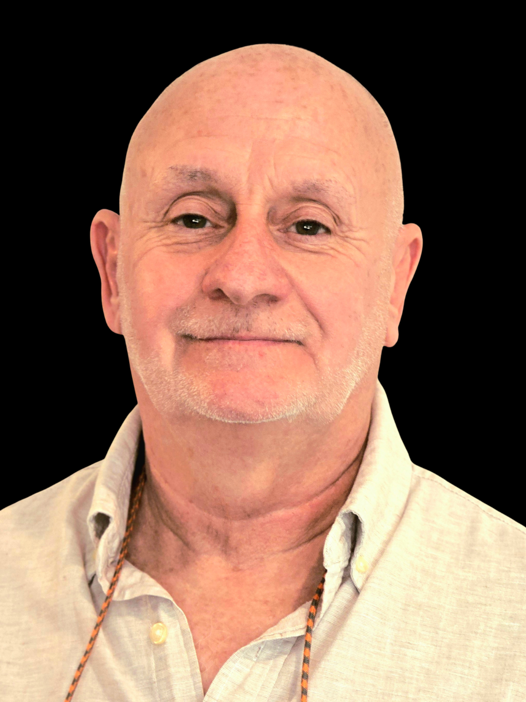 Portrait of an older man with a bald head, light skin, and a goatee, wearing a green polo shirt against a black background.