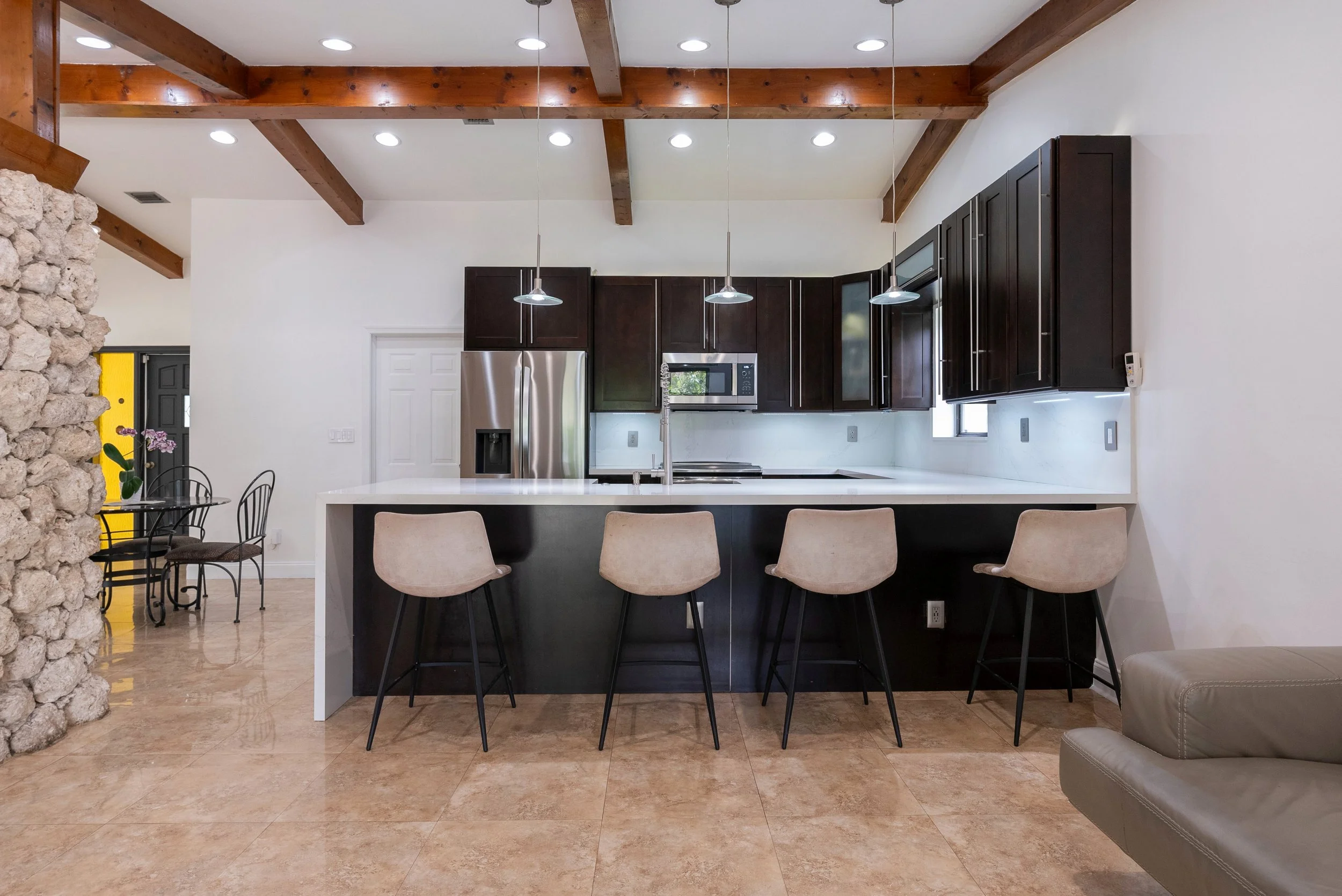 Modern Miami home kitchen with dark wood cabinetry, large white island, exposed wood beams and bar seating.