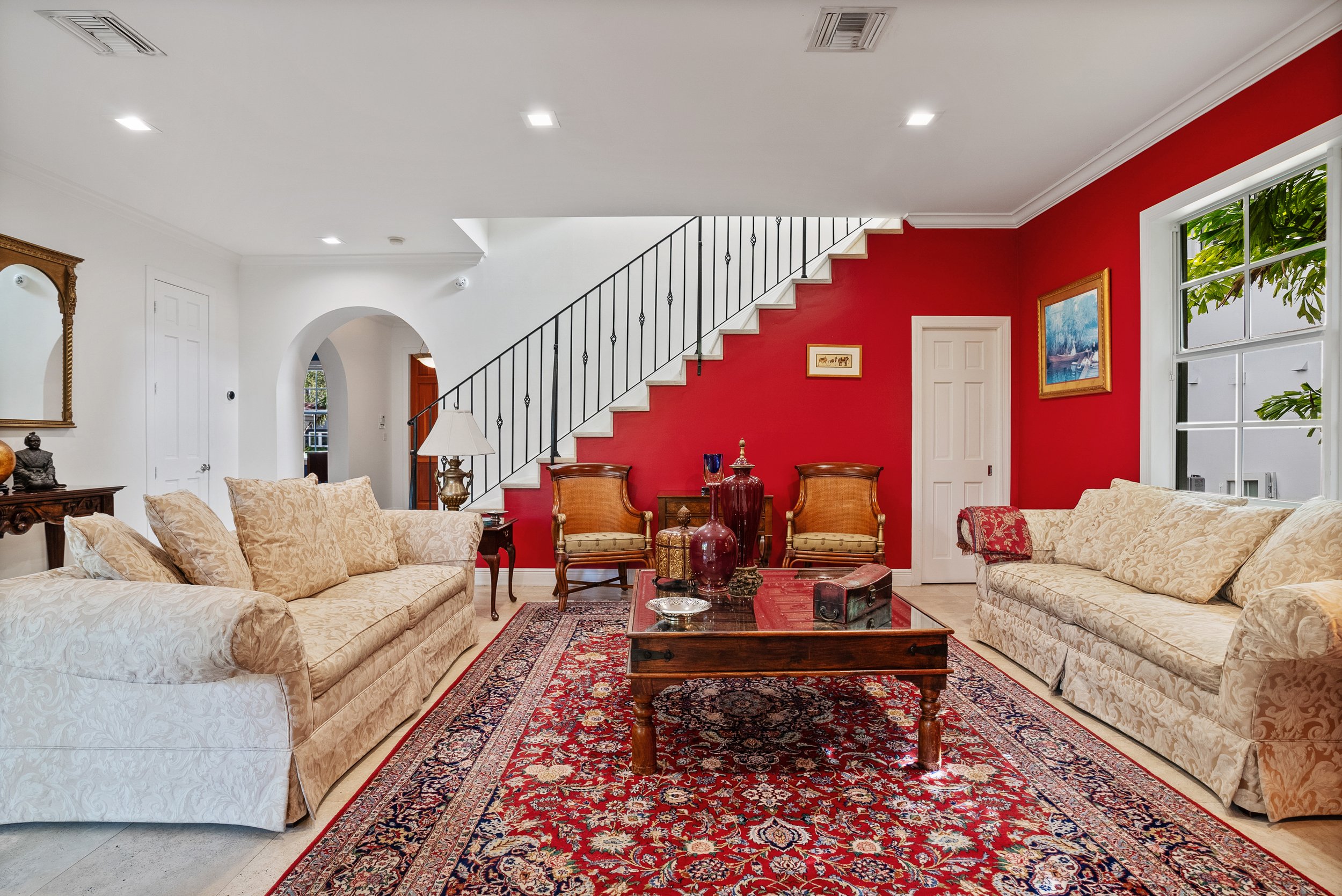 Key Biscayne home living room with elegant furnishings, red accent wall and staircase.
