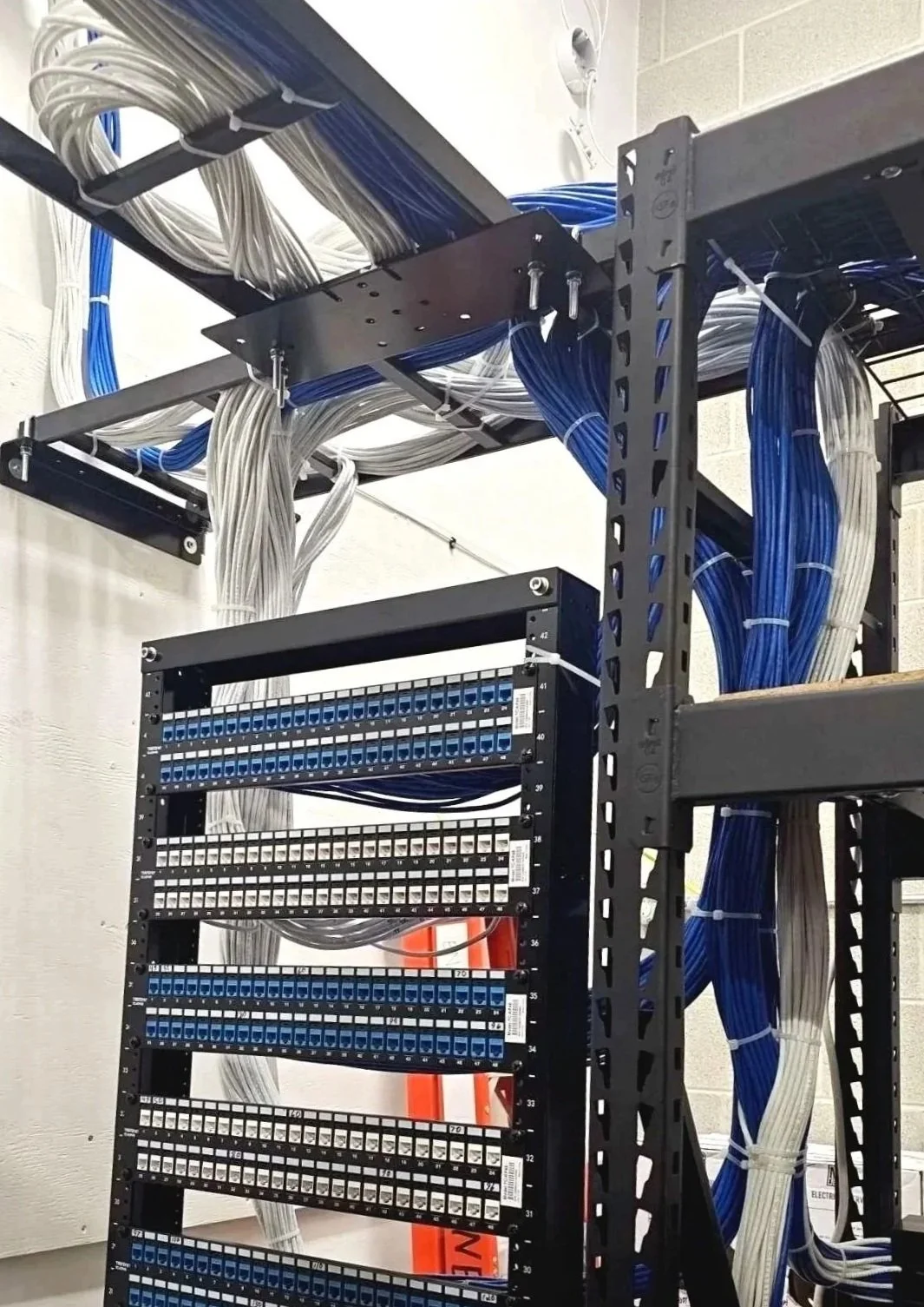 Network server rack with organized blue and white Ethernet cables set up by AKC Electrical, connected to patch panels mounted on a black metal frame