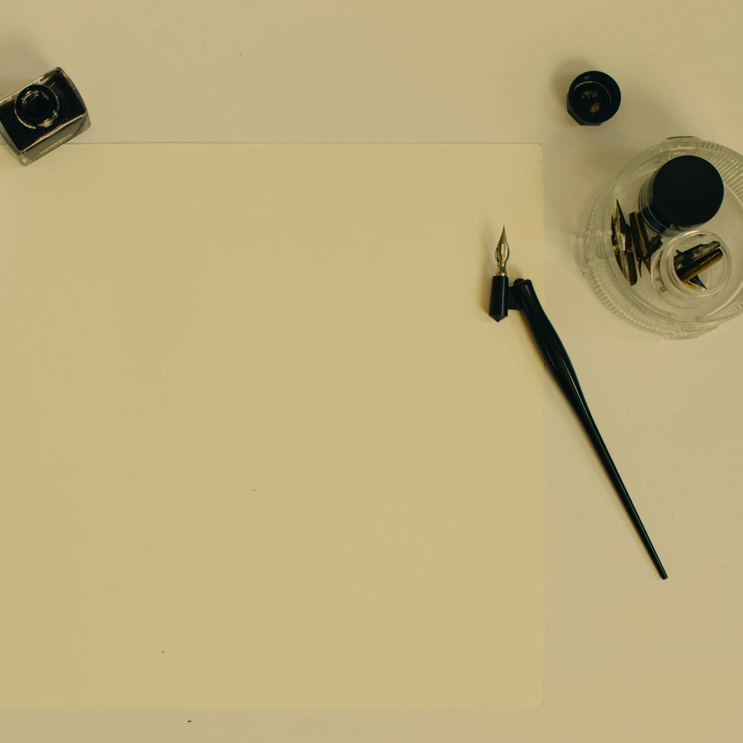 Writing and calligraphy tools on a table, including a dip pen, ink bottle, and a container holding additional nibs.
