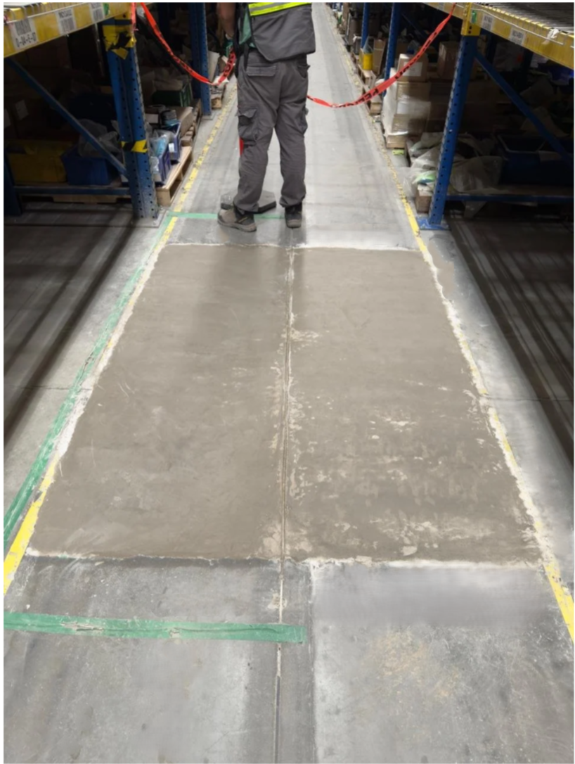 A person working on a concrete floor in a warehouse aisle, with red caution tape cordoning off the area.