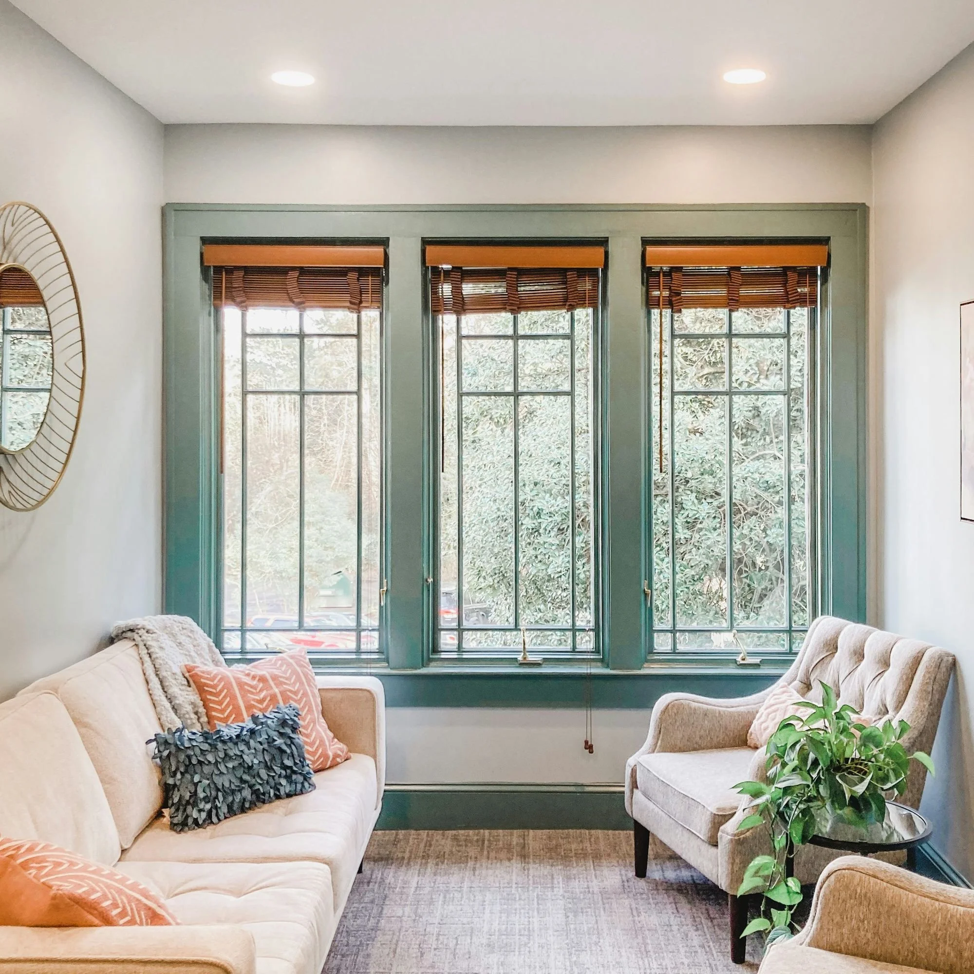 Living room with beige sofas, threw pillows, large window with blinds, and a potted plant.