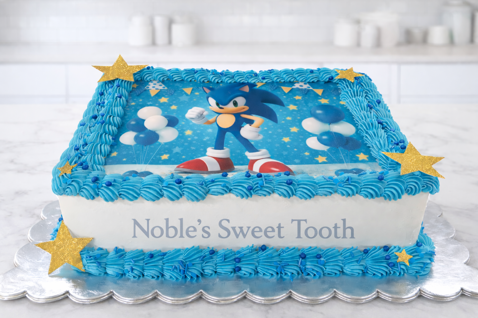 A birthday cake decorated with a Sonic the Hedgehog theme, featuring an edible Sonic image on top, blue frosting, and gold star decorations, with the message "Noble's Sweet Tooth" on the side.
