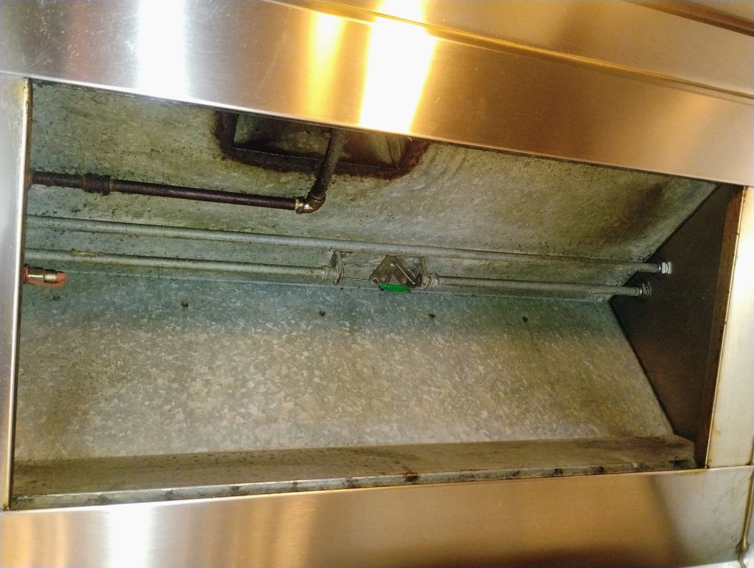 Empty commercial kitchen oven or microwave with visible metal interior and some pipes or wires inside.