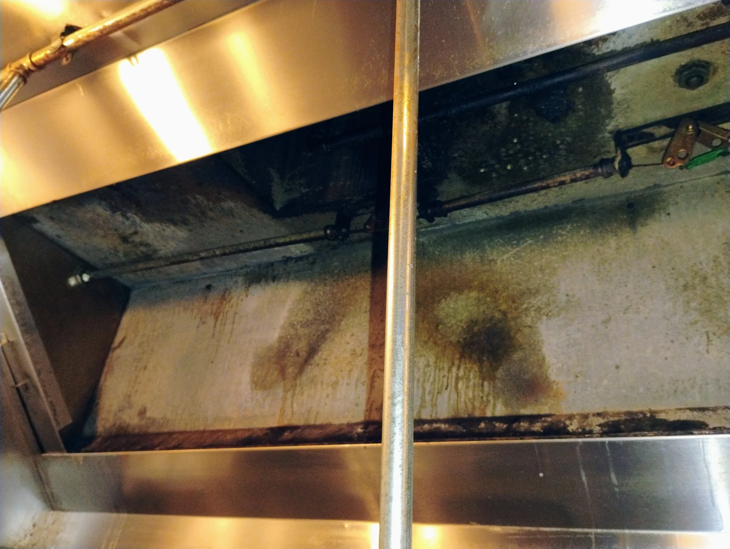 Inside a commercial kitchen oven with visible dirt, grime, and oil stains on the surface and a metal divider in the middle.