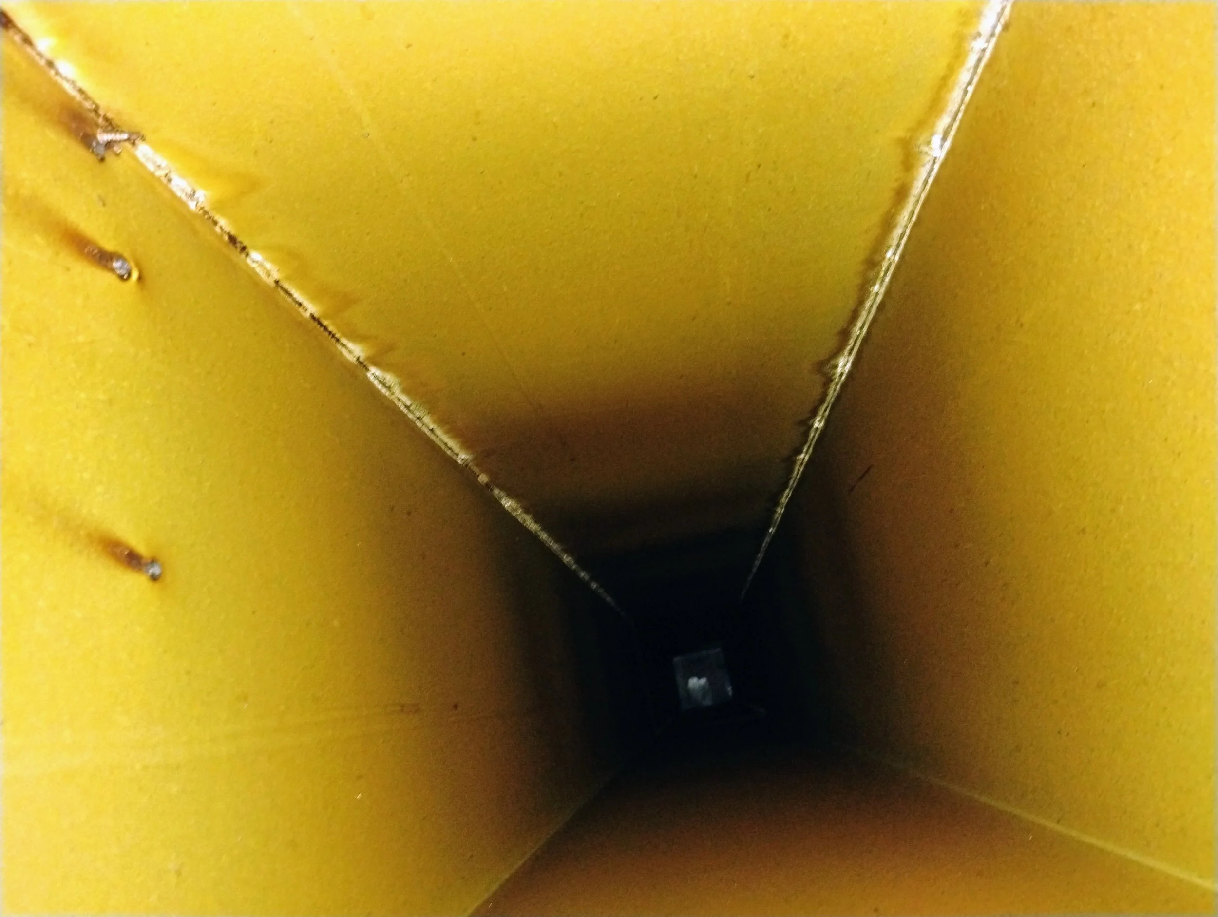 Inside view of a tall, yellow, metal chimney or pipe extending into darkness.