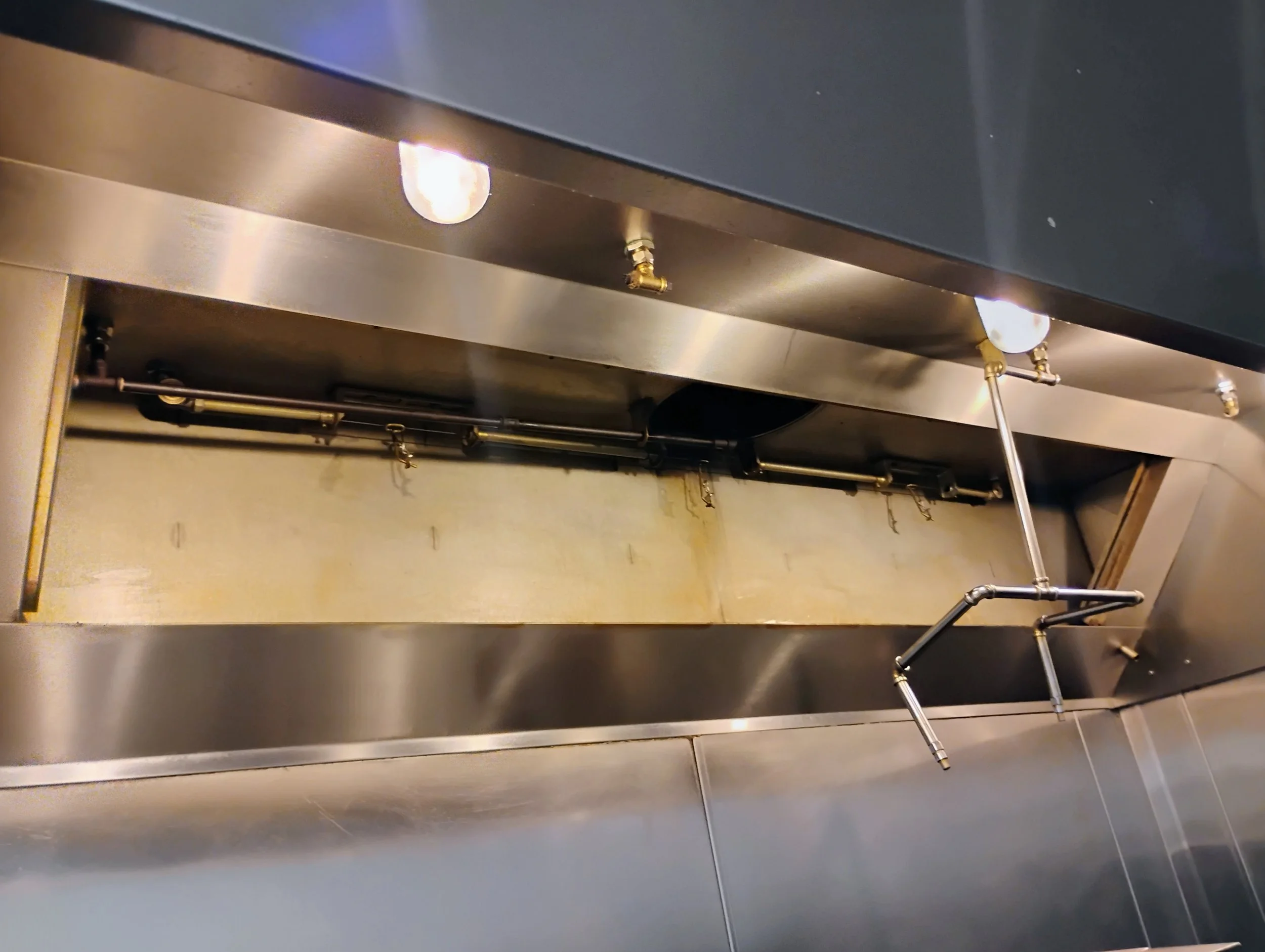 Inside a stainless steel industrial oven or furnace, showing the interior with pipes and valves, and a brass pipe with a lever extending from the side.