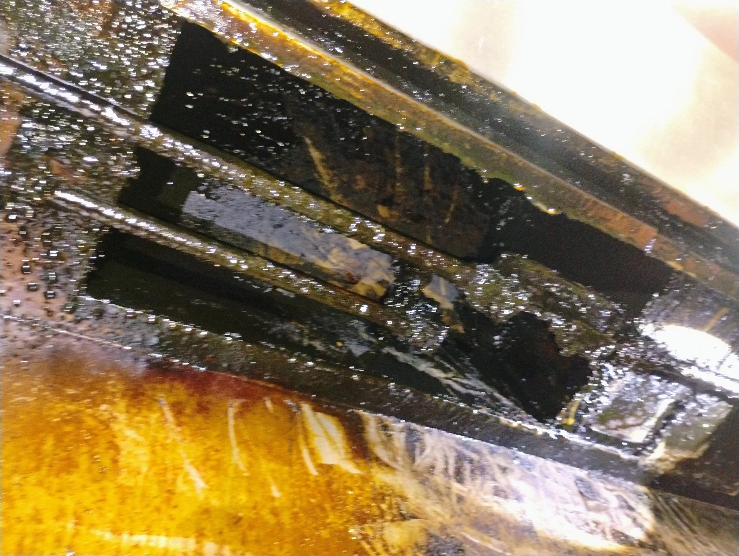 Close-up of a rusty metal object covered in black oil or grease.