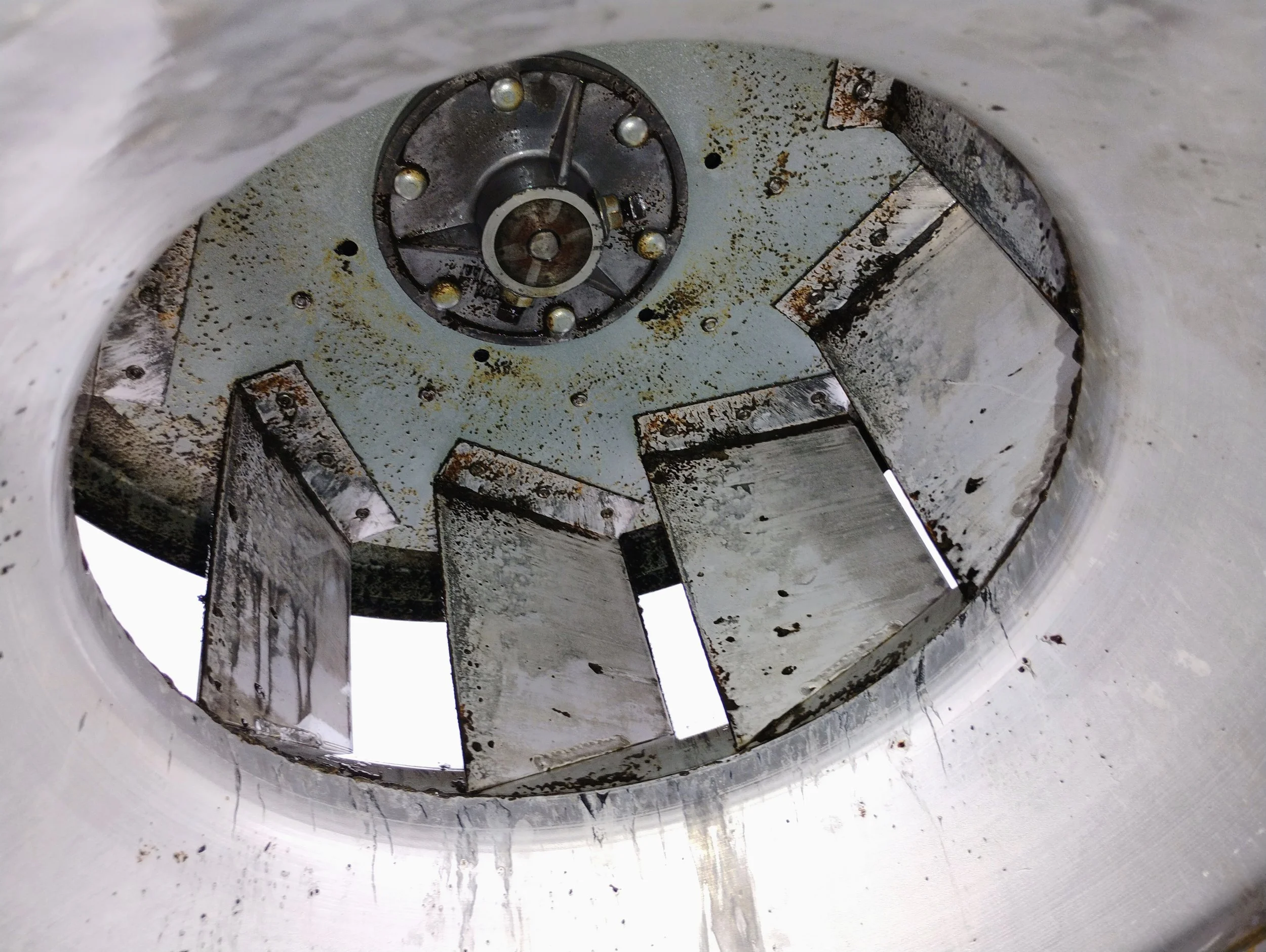 Inside view of a cylindrical metal tank with slanted metal baffles and a central mechanical component, showing signs of rust and dirt buildup.