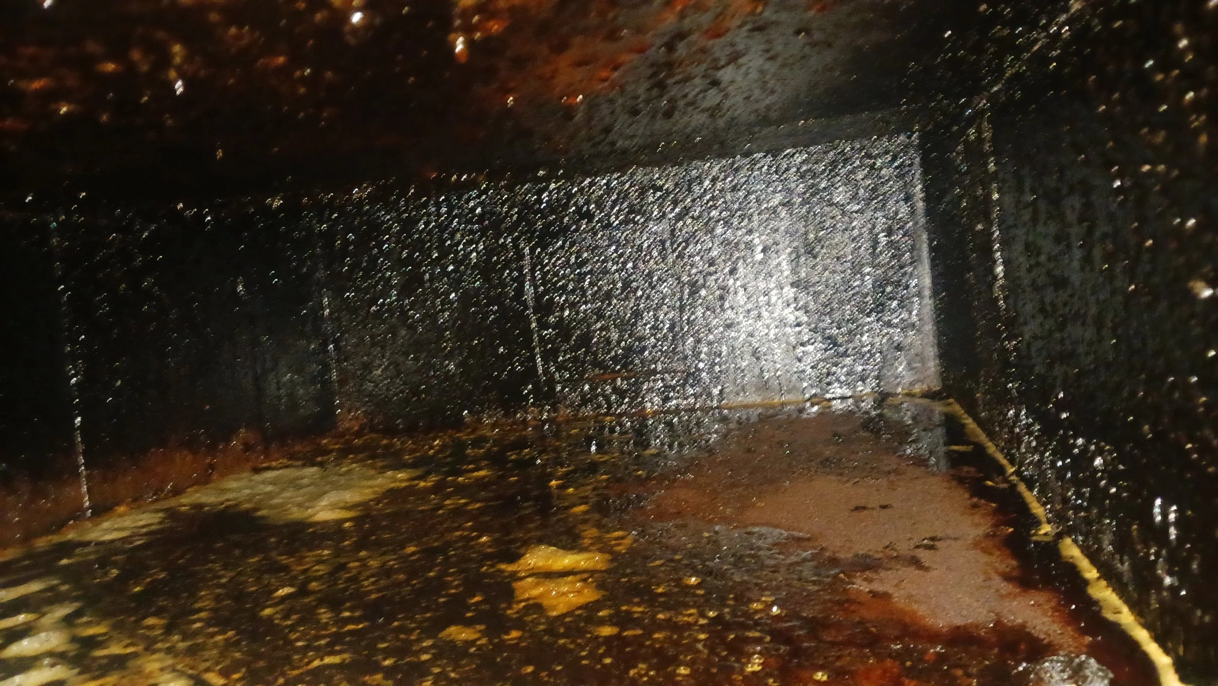 Close-up image of a rusty, greasy, and oily metal surface with black and brown grime, water marks, and some peeling paint.