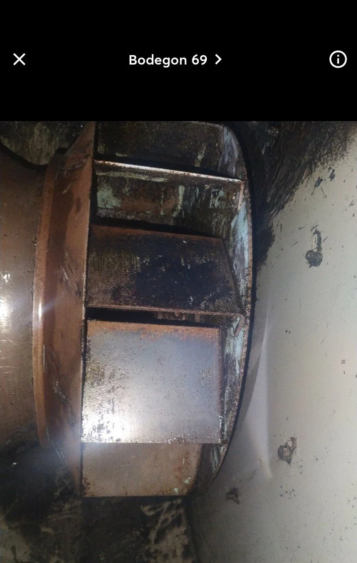 A rusty, metal storage shelf with three open compartments, situated against a damaged and dirty wall. The shelf shows signs of corrosion and grime.