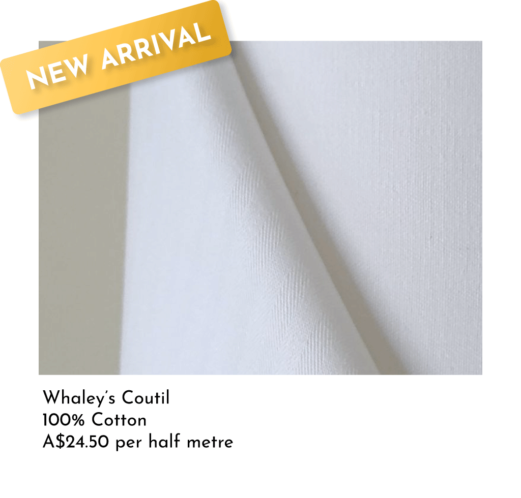 Close-up of white cotton fabric with a yellow "New Arrival" label in the top left corner. Text below describes the fabric as Whaley's Couture, 100% cotton, priced at A$24.50 per half meter.