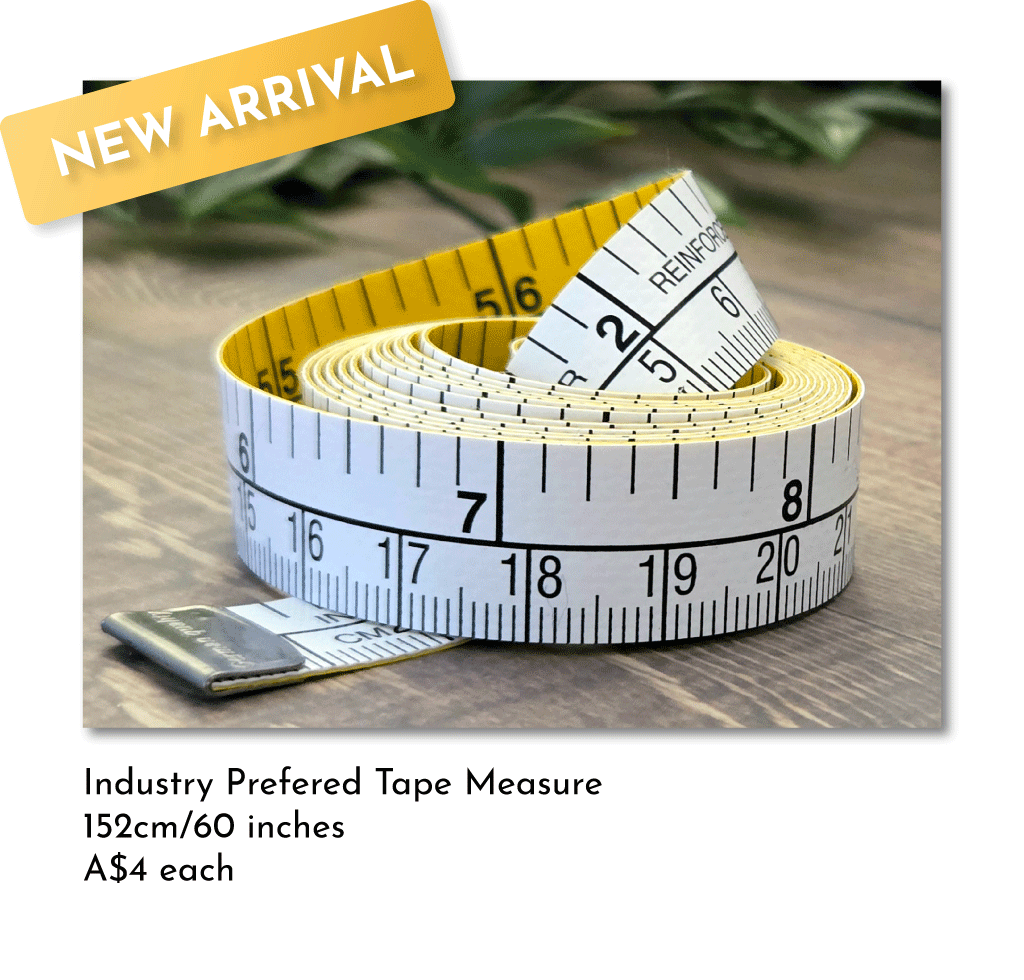 Rolled yellow and white measuring tapes with black measurement markings, placed on a wooden surface. A tag overlay reads 'New Arrival'.