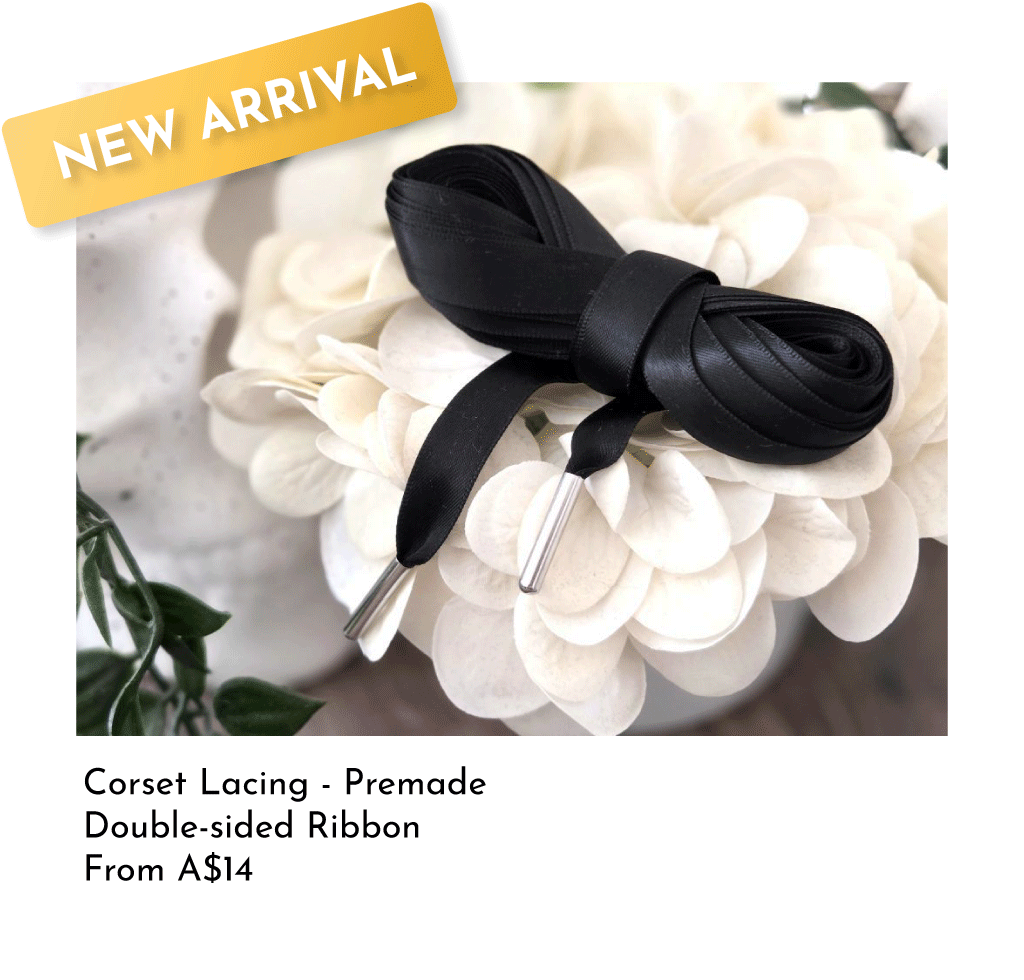 A black satin double-sided ribbon tied into a bow on white flower petals with green leaves in the background.