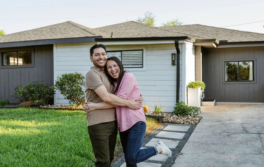 Happy couple hugging in front of their house with a manicured lawn.