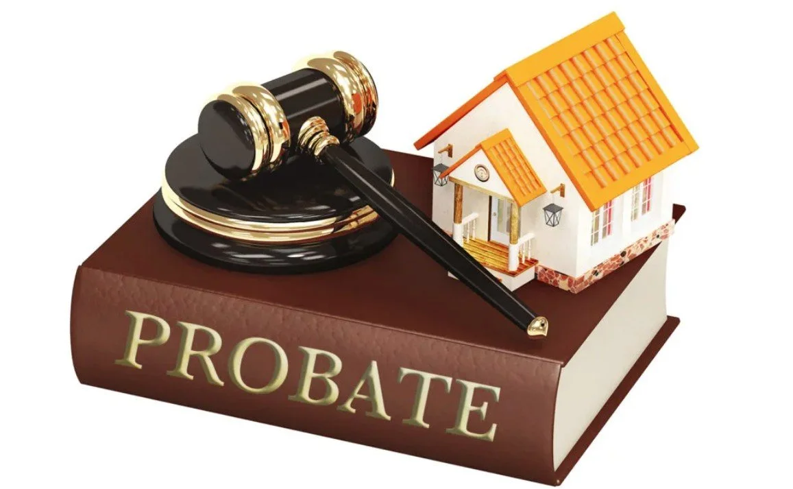 A gavel resting on a large book with the word "PROBATE" on the spine, a miniature house placed on the book next to the gavel.