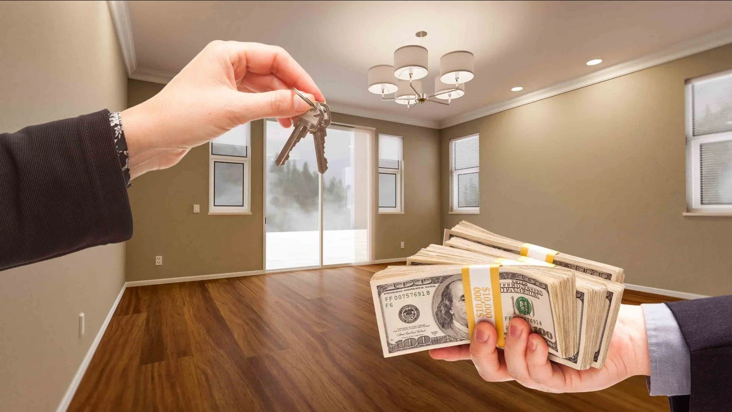 A person holding a bunch of hundred-dollar bills and another person holding keys in a modern, empty living room with hardwood floors and large windows.