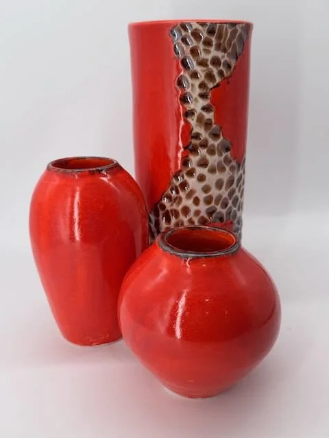 Three red ceramic vases, one tall with honeycomb pattern, two smaller round with smooth surfaces.