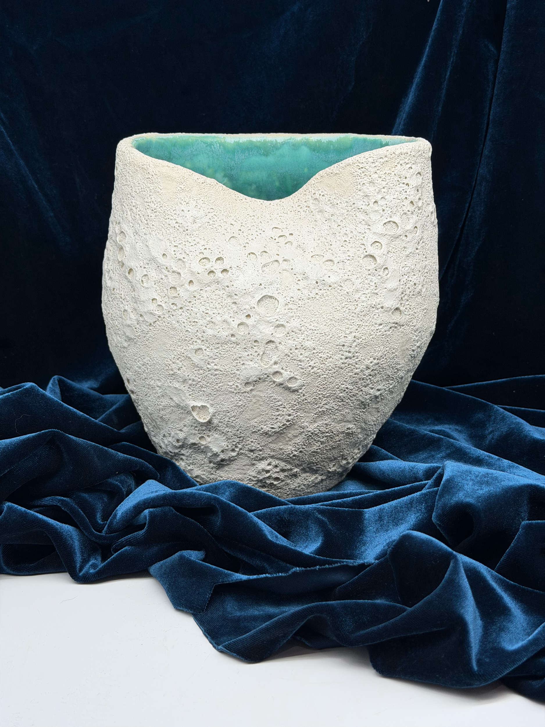 A textured white piece of art or pottery with holes, placed on dark blue velvet fabric.