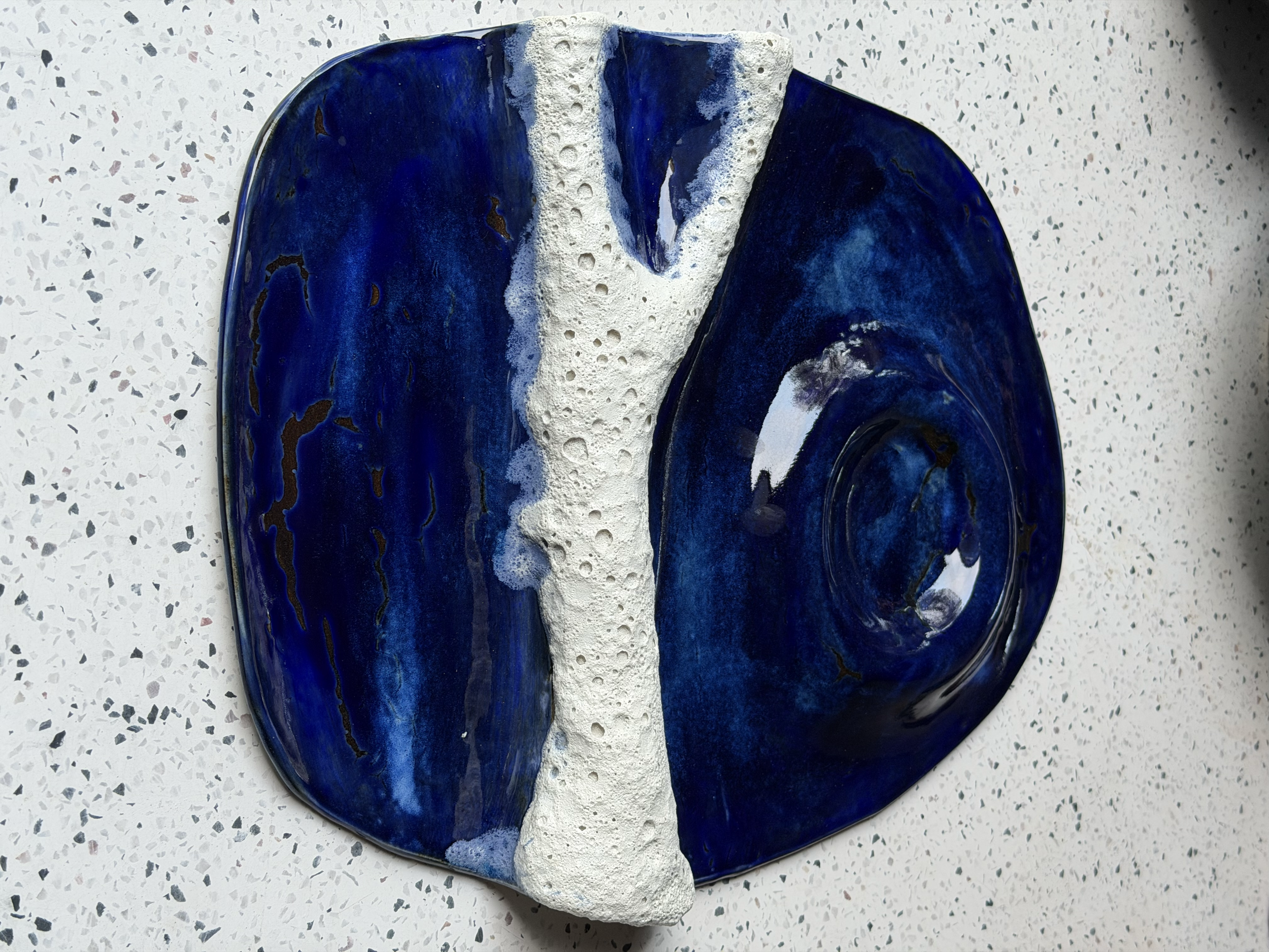 A decorative ceramic plate with dark blue glaze and a textured white center, placed on a white speckled countertop.