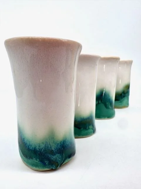 Set of three ceramic cups with a gradient glaze from beige at the top to blue and green at the bottom, arranged in a row.