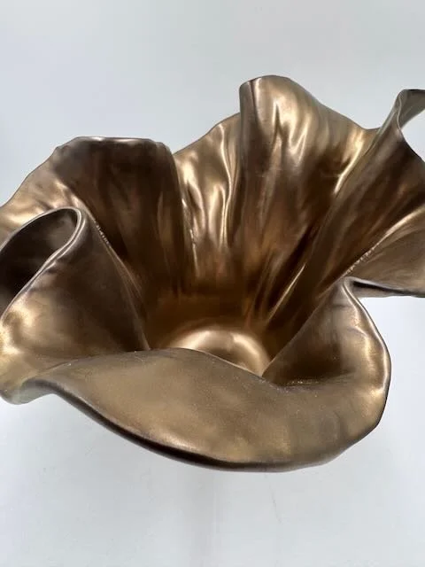 A decorative metallic gold bowl with irregular, ruffled edges, seen from above.