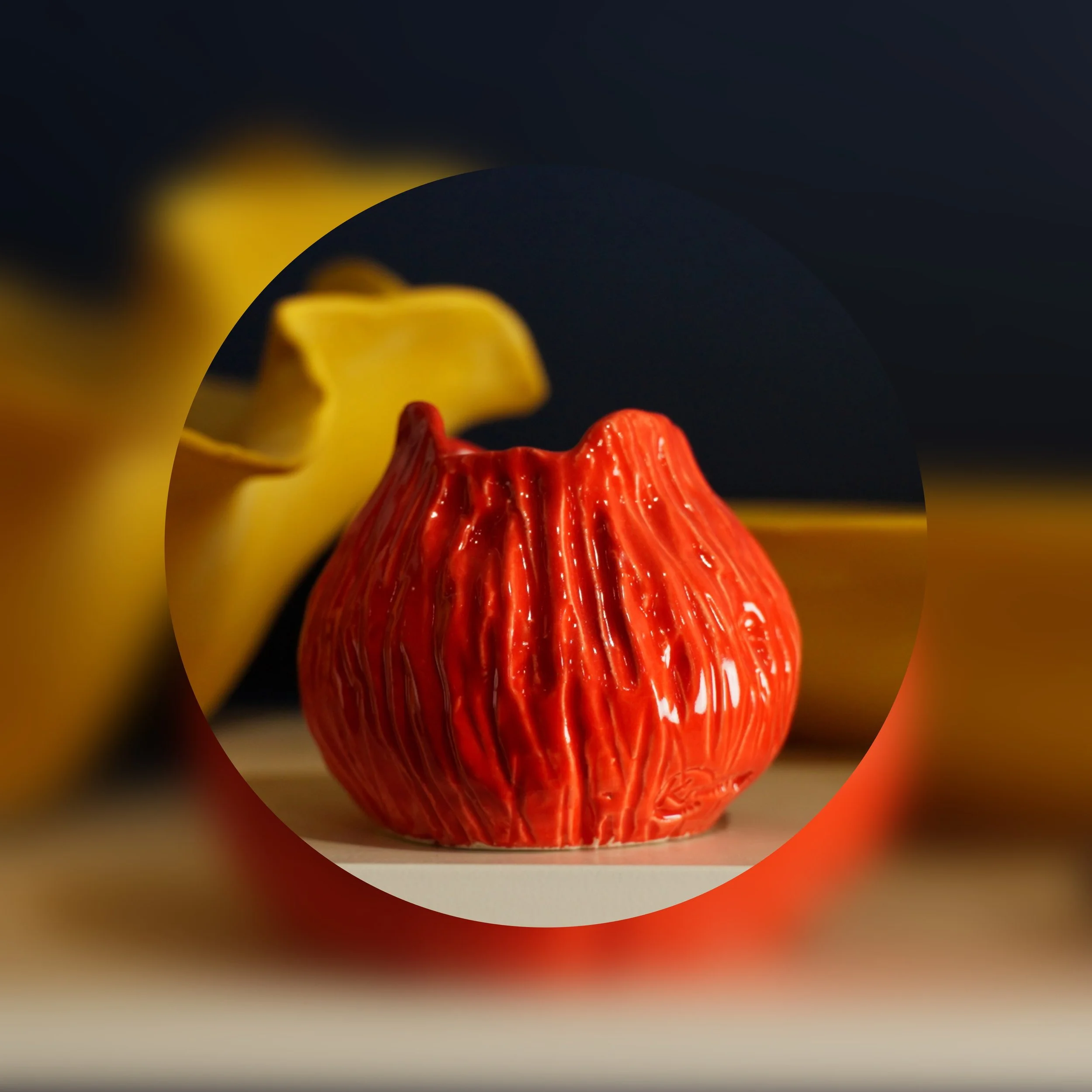 Close-up of a colorful, textured ceramic sculpture with red, yellow, and orange hues on a gray surface against a dark background.