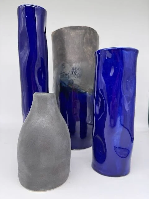 Four vases, two in cobalt blue glass and two in gray stone or ceramic, arranged against a white background.