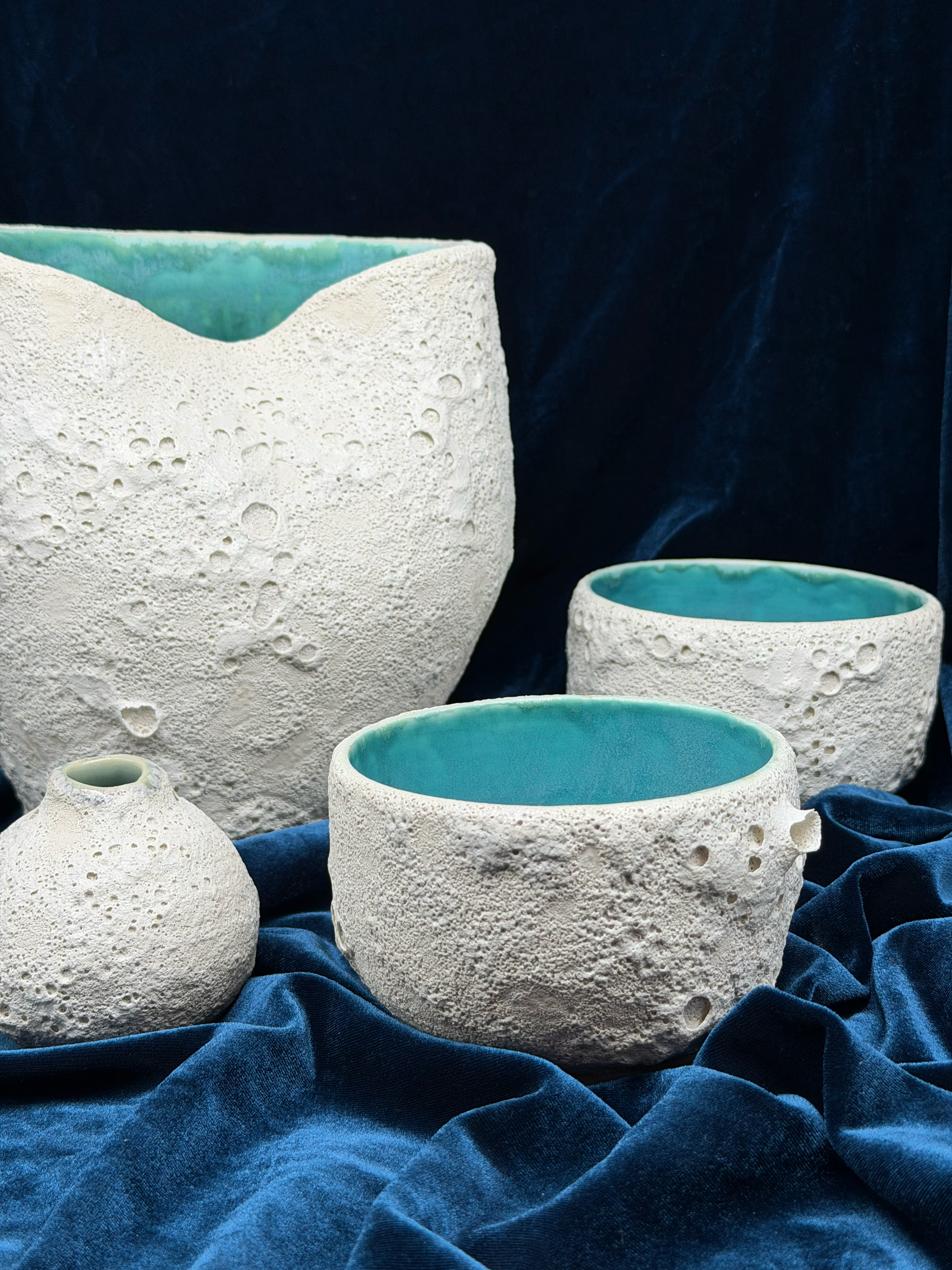 Close-up of white textured volcanic rock with a hollow center lined with turquoise, set against dark blue velvet fabric.