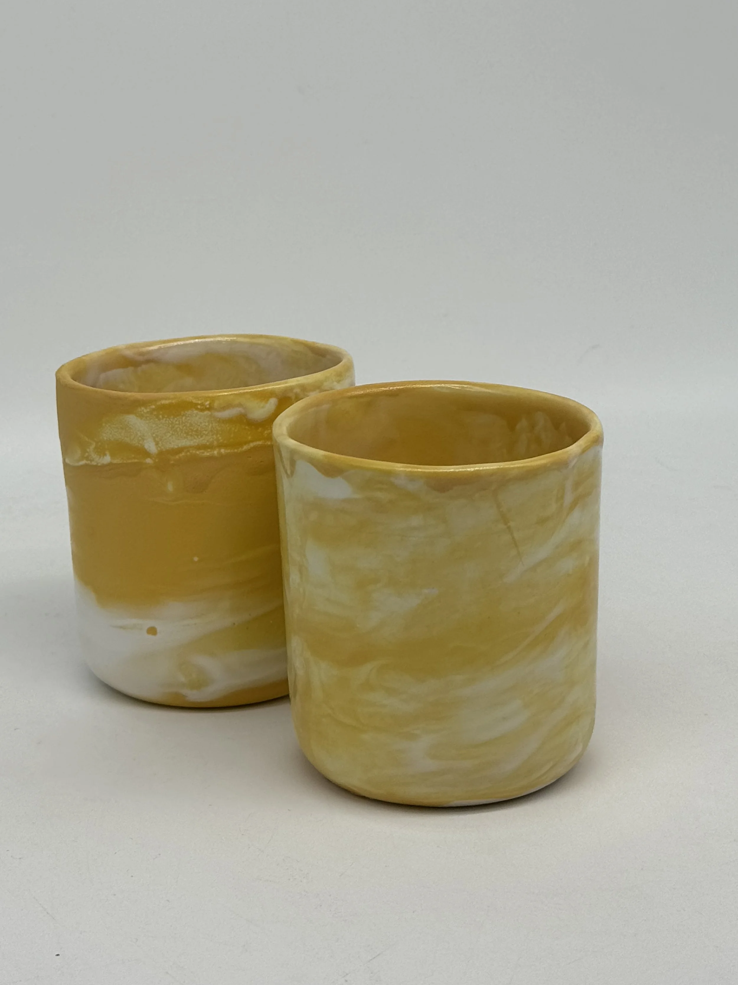 Two yellow and white marble-patterned candles on a white surface with a plain white background.