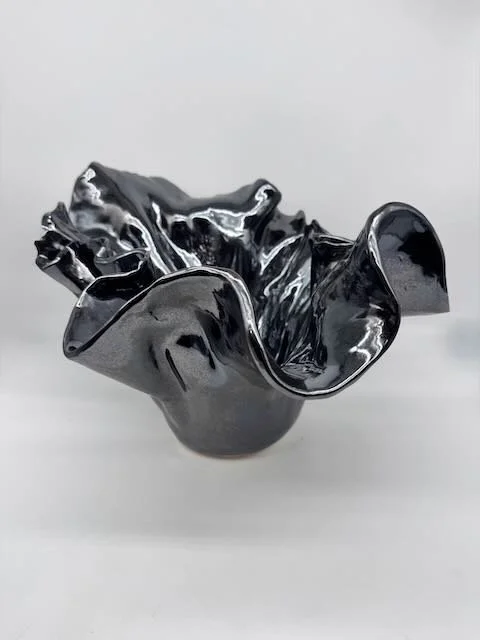A metallic, black, irregularly shaped ceramics bowl with ruffled edges.