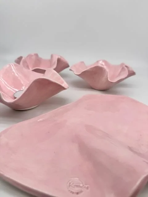 Decorative pink ceramic bowls and a pink ceramic plate on a white surface.