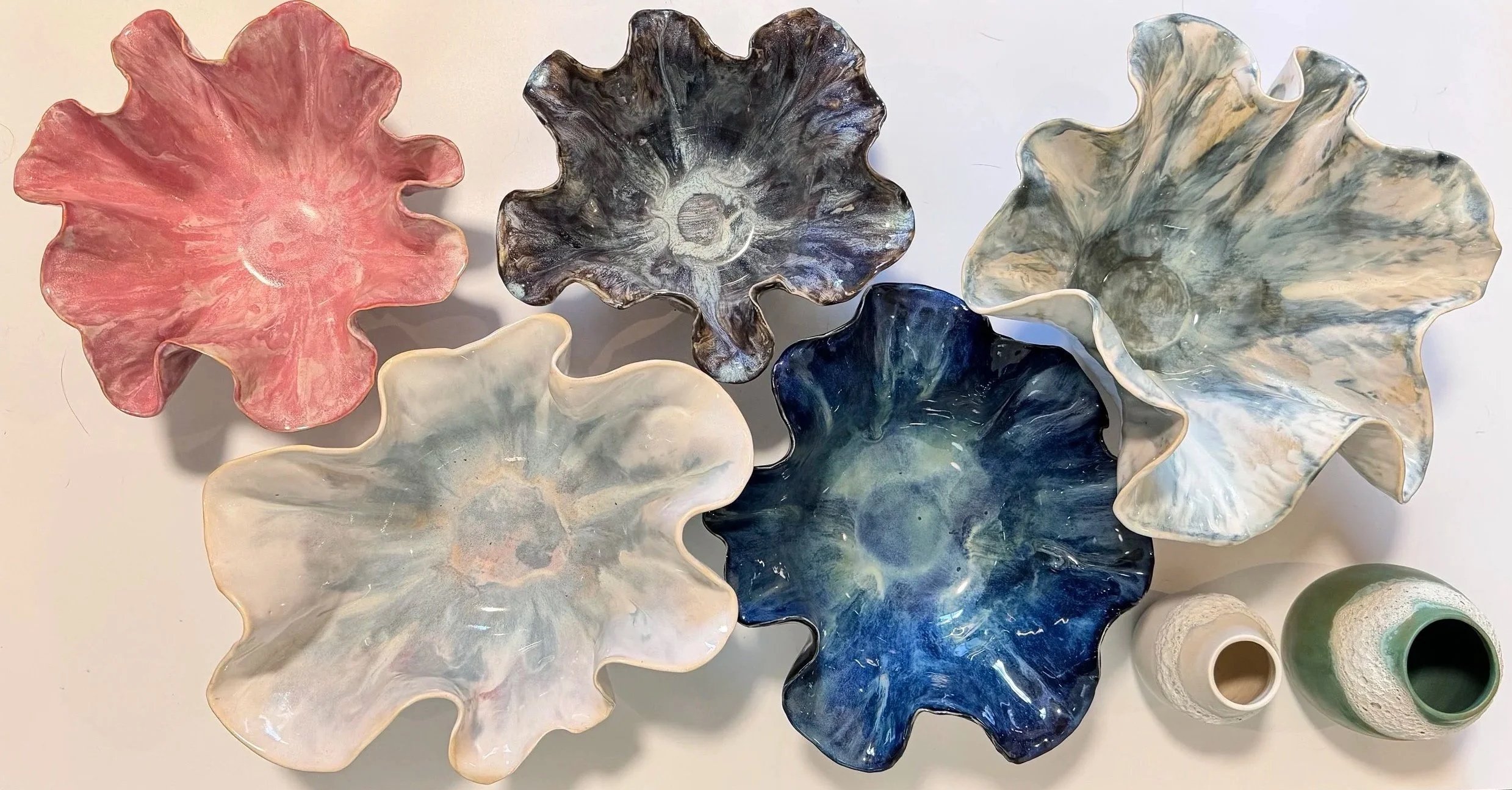 Colorful ceramic bowls with wavy edges arranged on a white surface, along with a few small ceramic vessels.